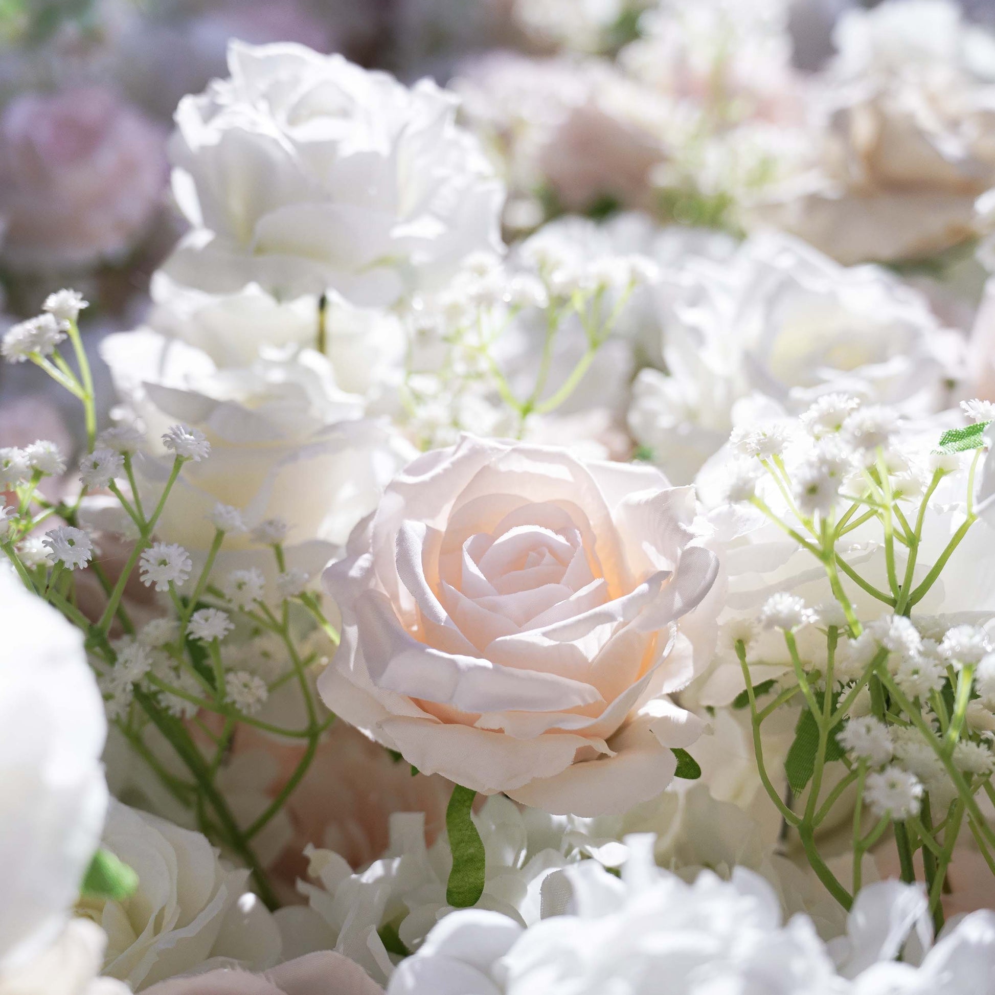 This close - up image captures a section of a floral backdrop. The main flowers are artificial roses in shades of white and soft pink, interspersed with delicate sprigs of baby's - breath - like greenery. The color palette is light and airy, creating a romantic and elegant style, which is perfect for wedding or event decorations. 
