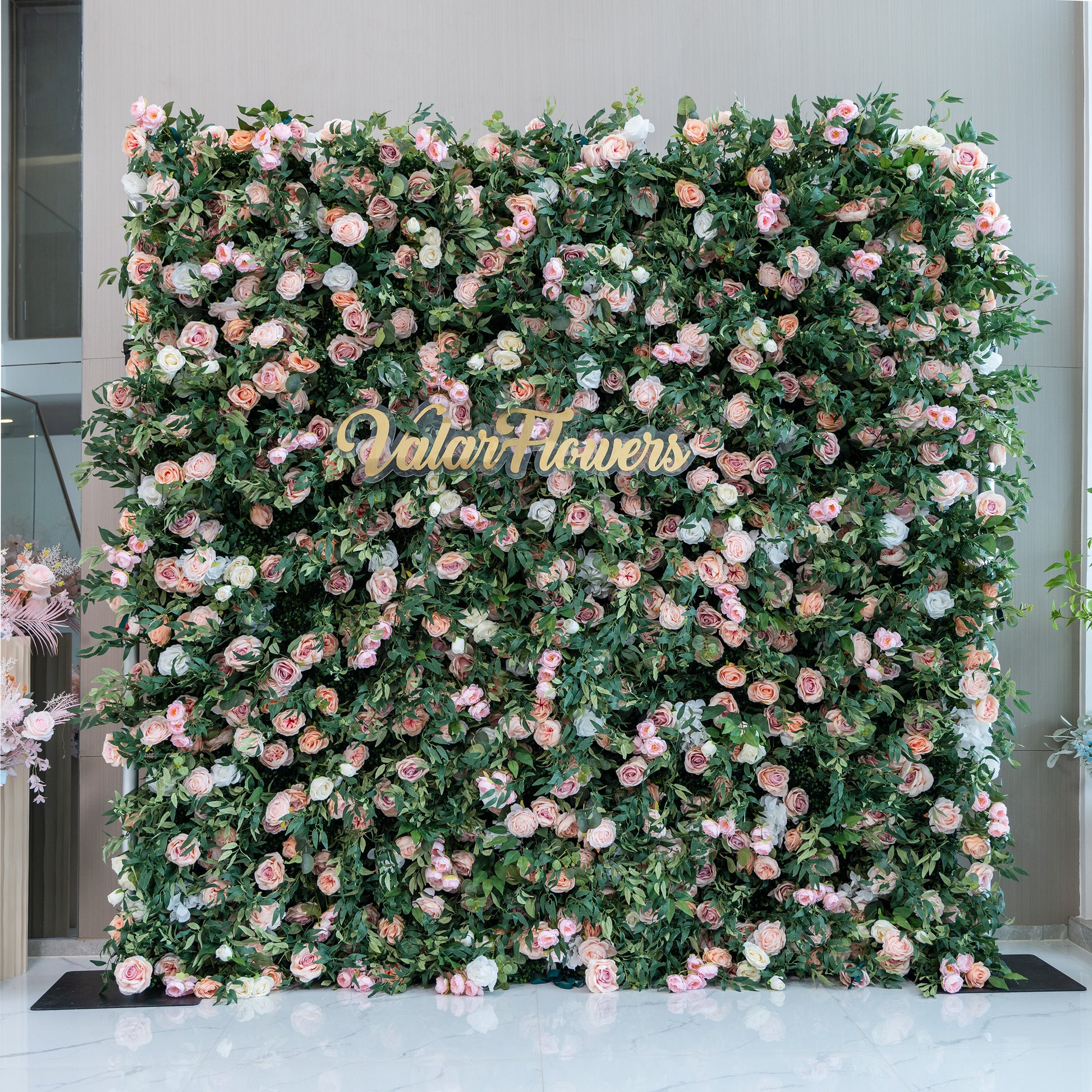 This photo features a large floral backdrop densely covered with pink and white roses, interspersed with lush green foliage. In the center, golden lettering spells out "ValarFlowers". Ideal for events like engagement parties or a "Blossom - filled Celebration", the soft - hued roses create a romantic and elegant atmosphere, making it a perfect decorative element for refined and joyous occasions. 