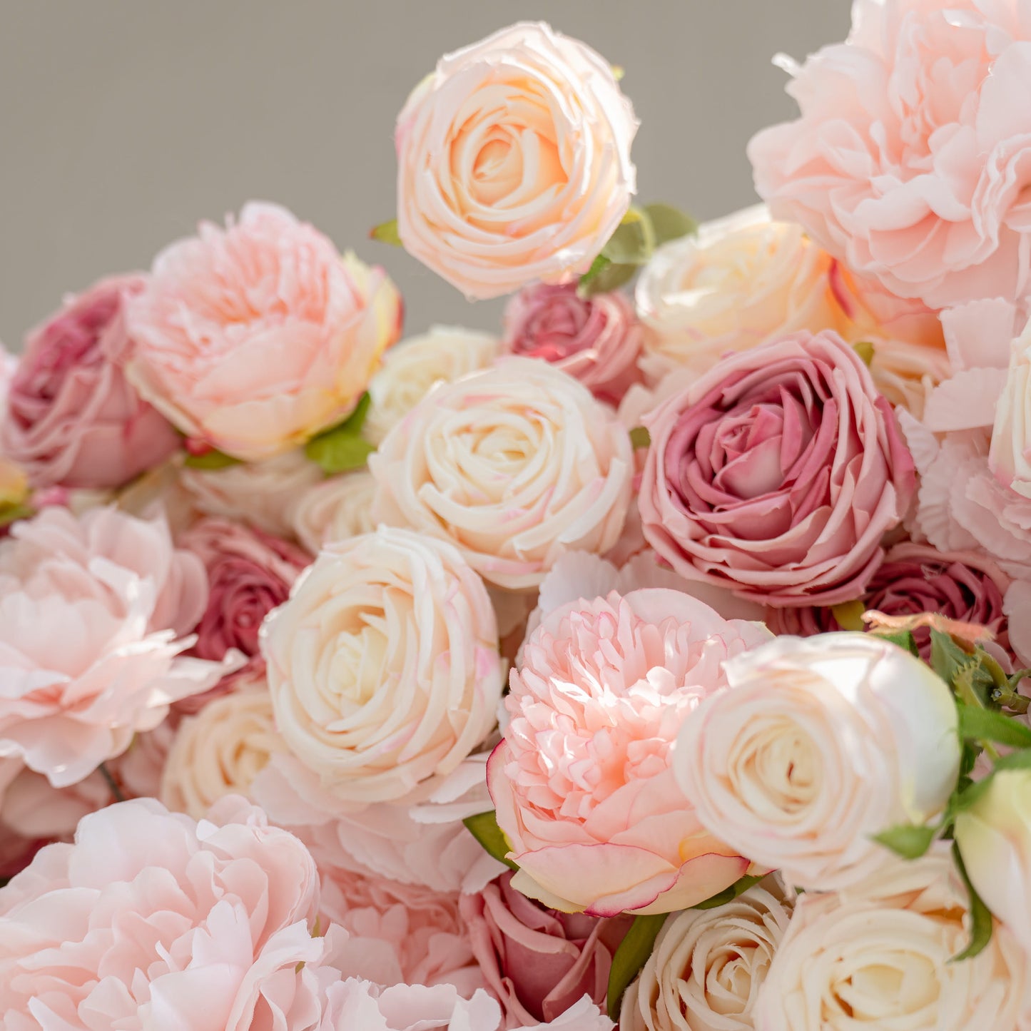 The image showcases a detailed arrangement of artificial flowers. Each petal's texture and color gradient, from soft pink to creamy white, is distinct. The realistic leaves and the precise placement of blooms highlight the craftsmanship.
