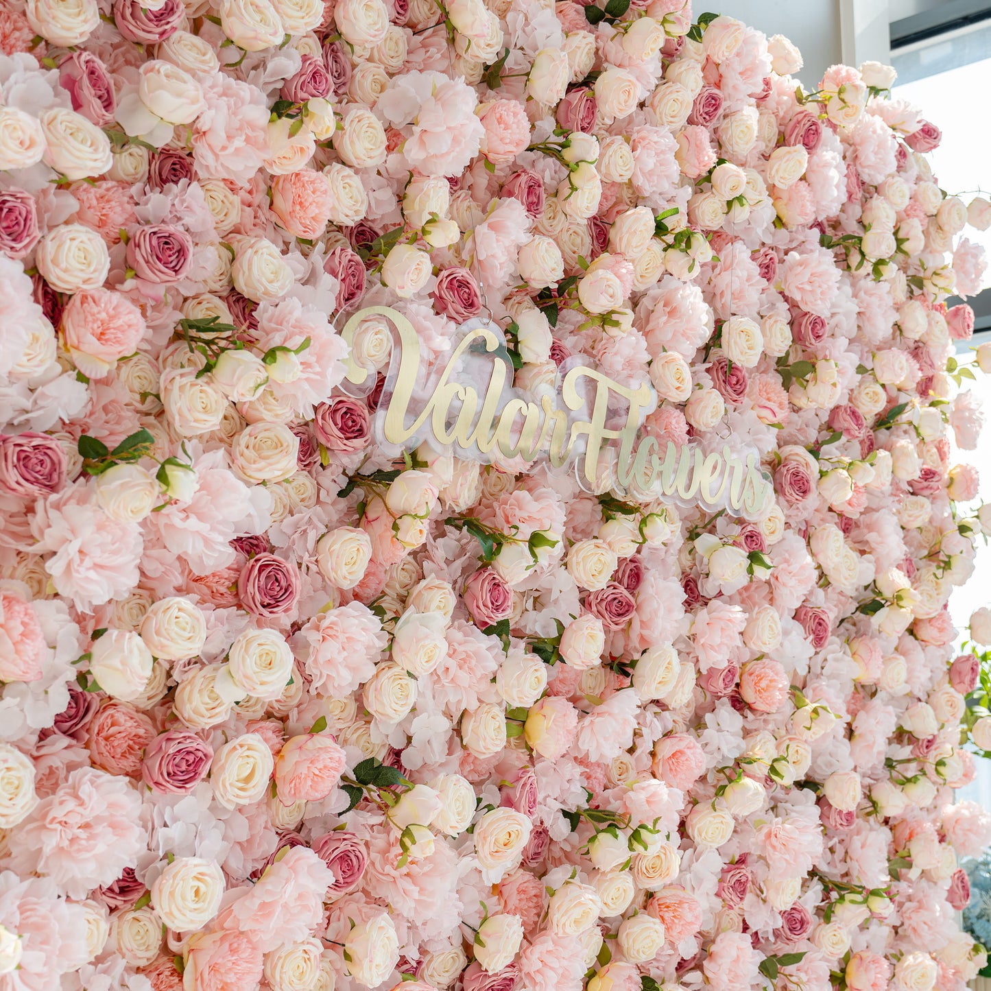 A beautiful flower wall composed of various pink and white roses and peonies. The words "Valar Flowers" are prominently displayed in the center, creating a romantic and elegant atmosphere.