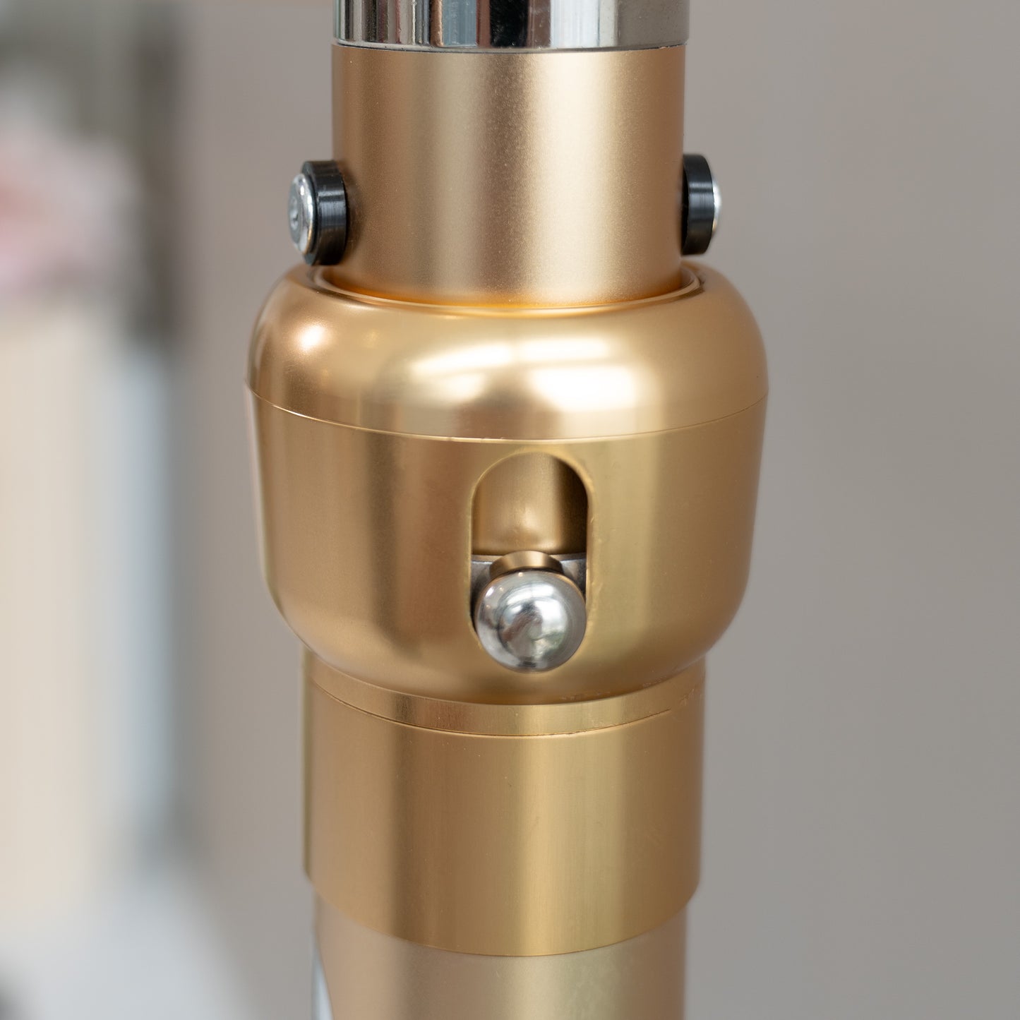 This image showcases a close - up of a metallic rod structure component. The piece is predominantly gold - colored with a smooth, polished finish. It features two black - capped screws near the top, likely for securing or adjusting purposes. There is also a prominent silver - colored spherical knob in the center, set within an oval - shaped cut - out. The design suggests it could be part of a stand or framework, perhaps for decorative or photographic equipment. 