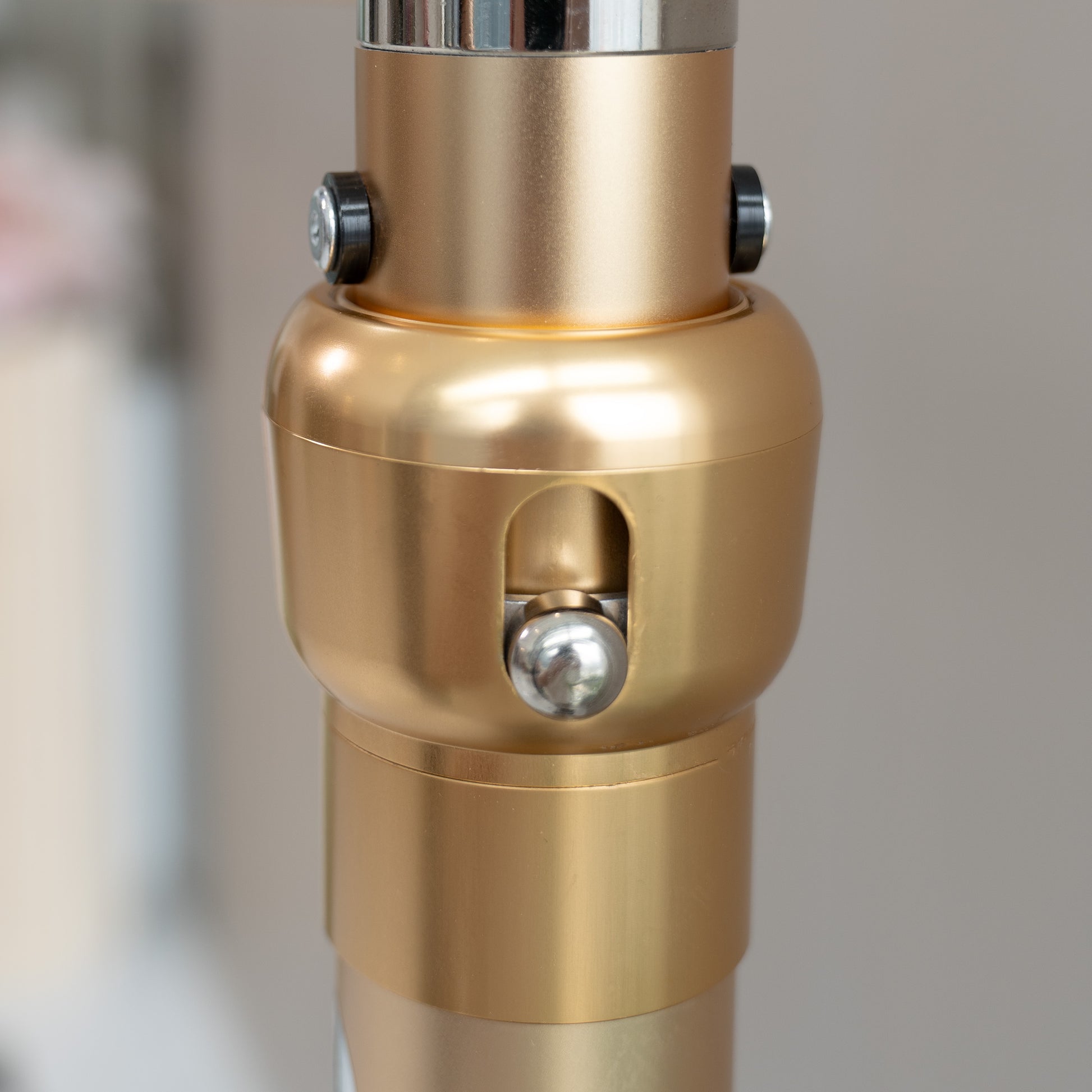 This image showcases a close - up of a metallic rod structure component. The piece is predominantly gold - colored with a smooth, polished finish. It features two black - capped screws near the top, likely for securing or adjusting purposes. There is also a prominent silver - colored spherical knob in the center, set within an oval - shaped cut - out. The design suggests it could be part of a stand or framework, perhaps for decorative or photographic equipment. 
