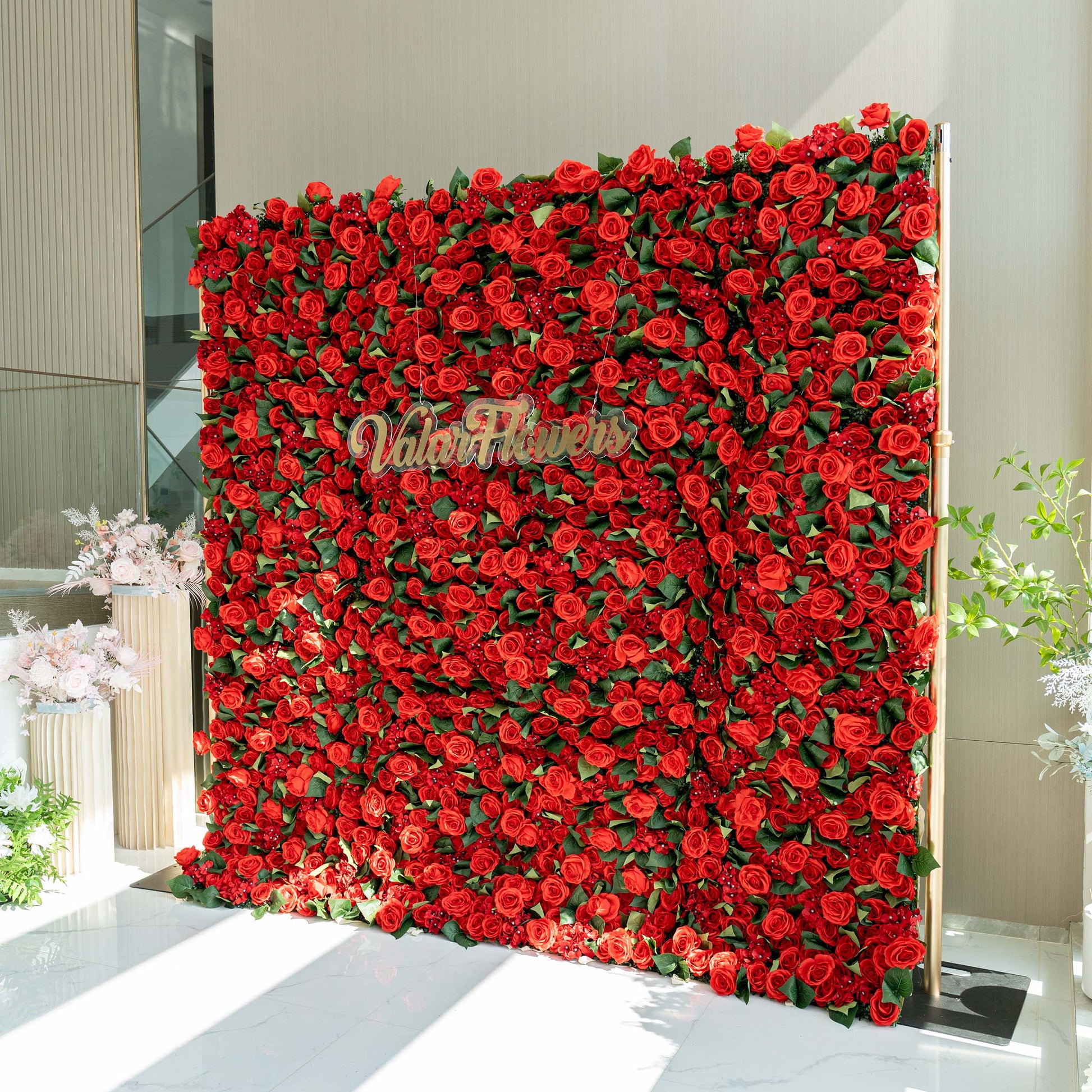 A lush floral wall by ValarFlowers, densely covered with vivid red roses and green leaves, making a striking decorative backdrop. 