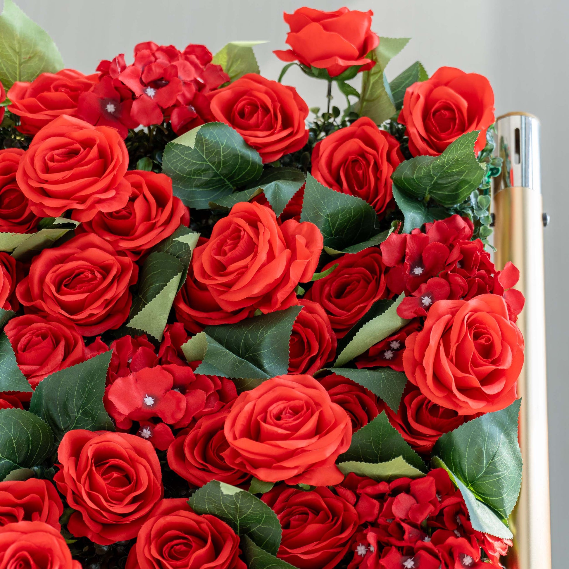 A close - up of a lush arrangement features vibrant red artificial roses interspersed with red hydrangeas and green leaves, creating a rich, eye - catching display. 