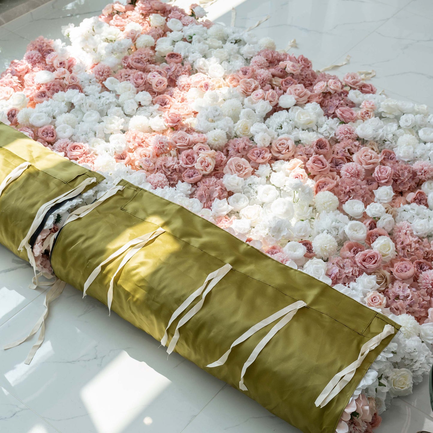 A rolled - up floral panel with a mix of white and pink roses and hydrangeas. The back features a green fabric with white ties, ready for setup. 