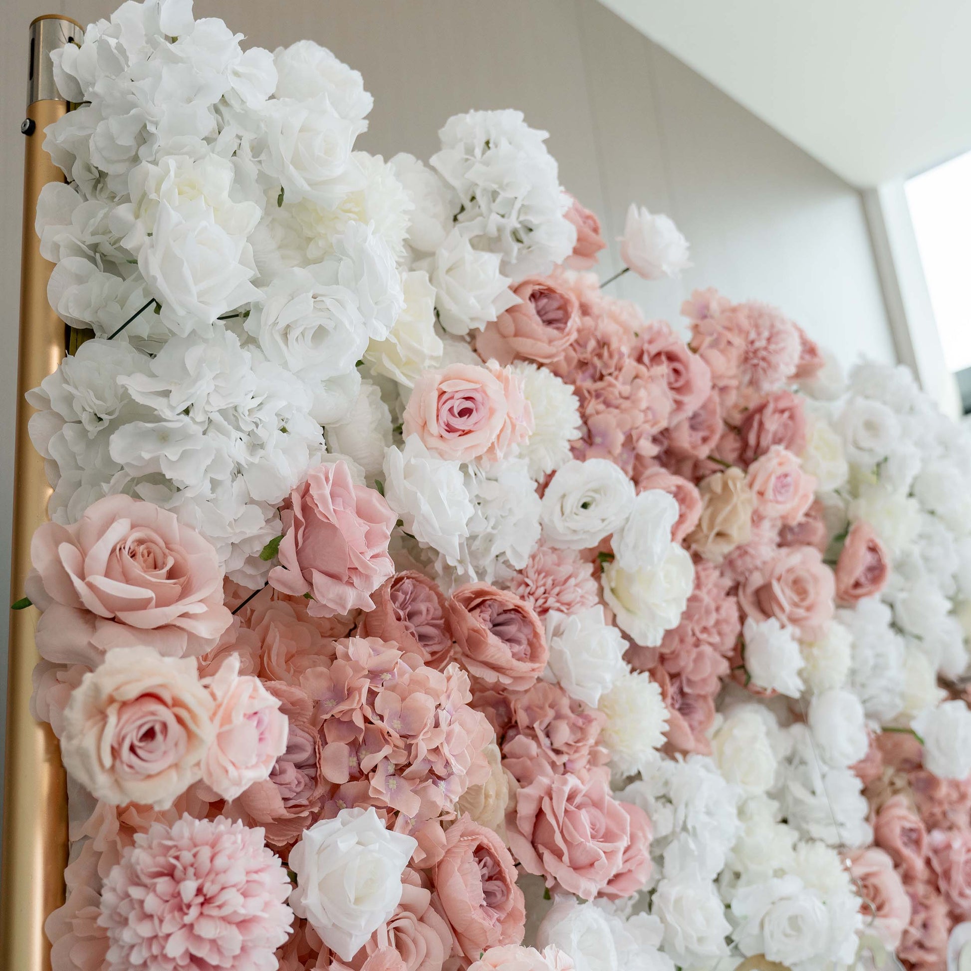 A close - up of a lush floral wall features an array of white and soft - pink artificial roses and hydrangeas, creating a romantic and elegant display. 
