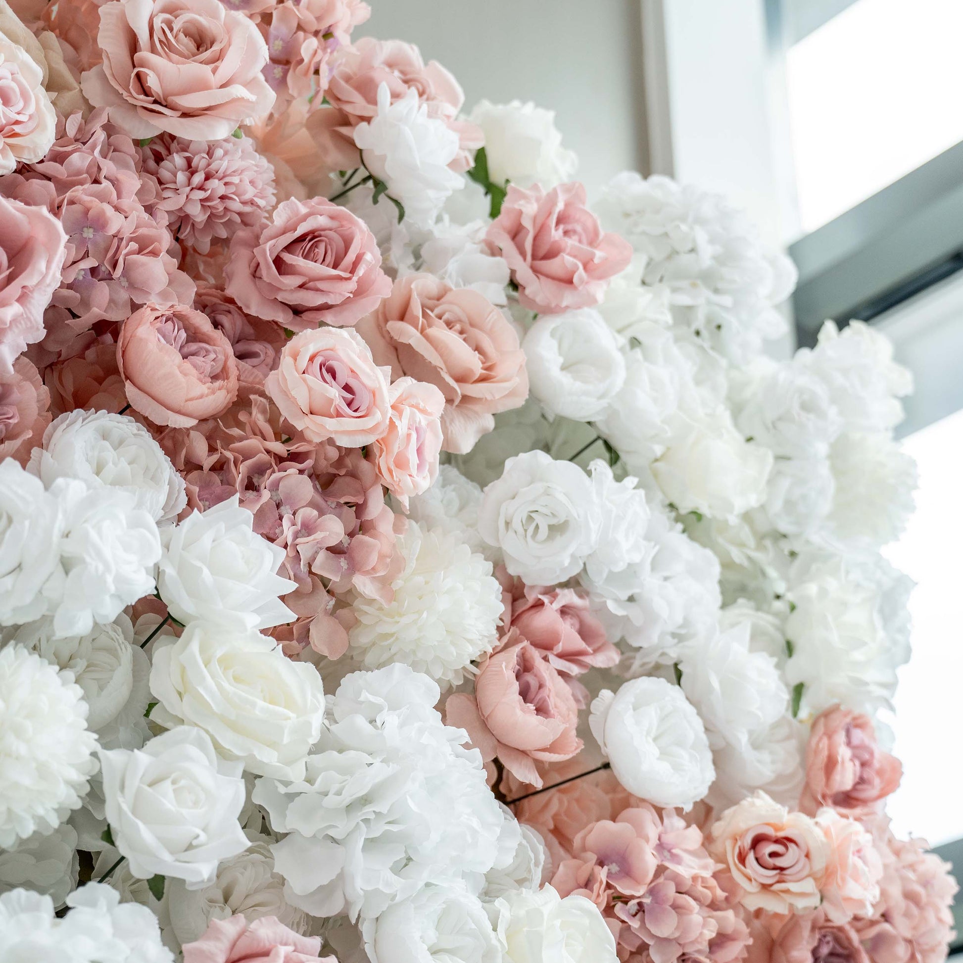 A close - up of a lush floral arrangement features an array of white and soft - pink artificial roses and hydrangeas, creating a romantic and textured display. 