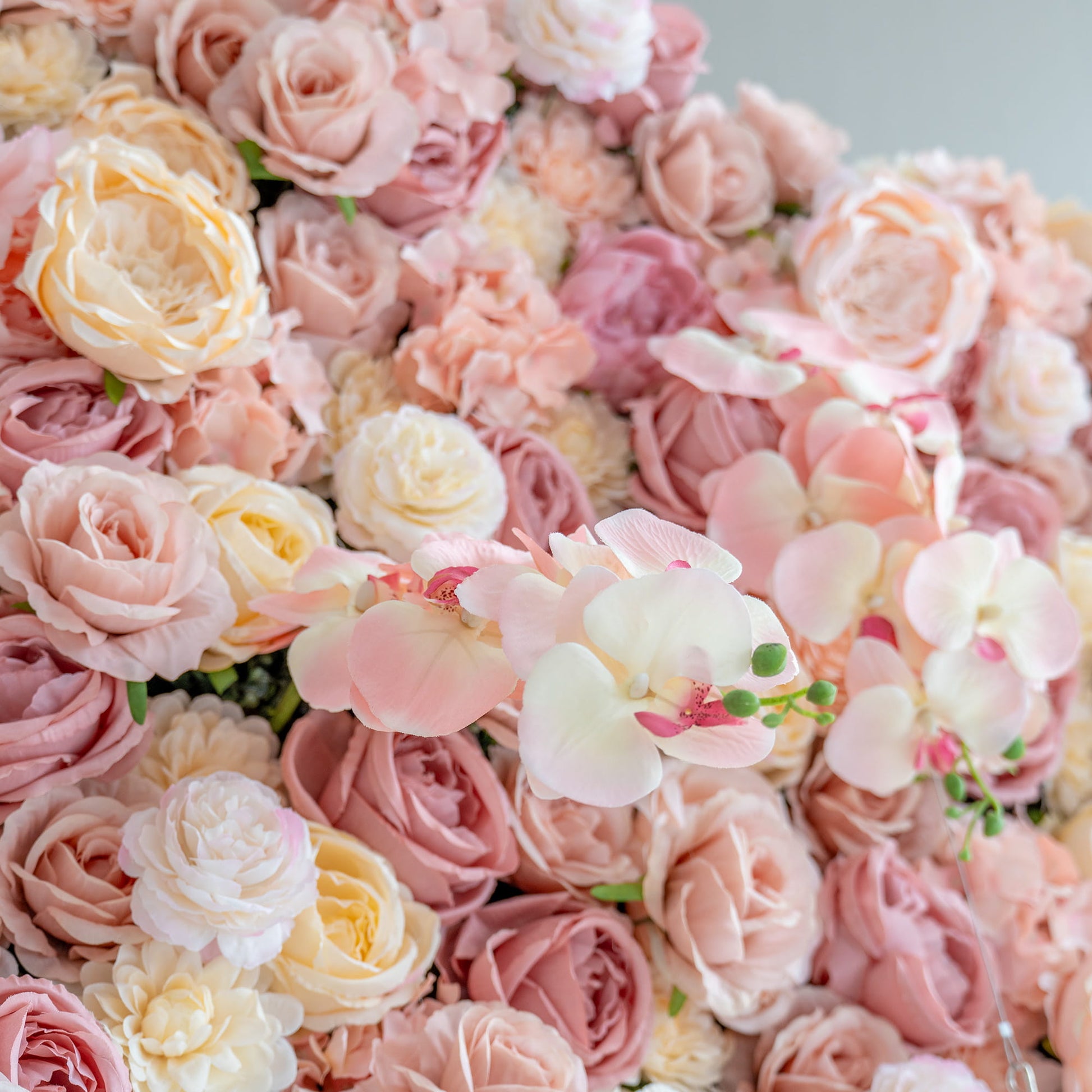 This close - up image features a blend of artificial roses and orchids. In soft pastel colors like pink, peach, and cream, the flowers create a romantic and elegant floral arrangement. 