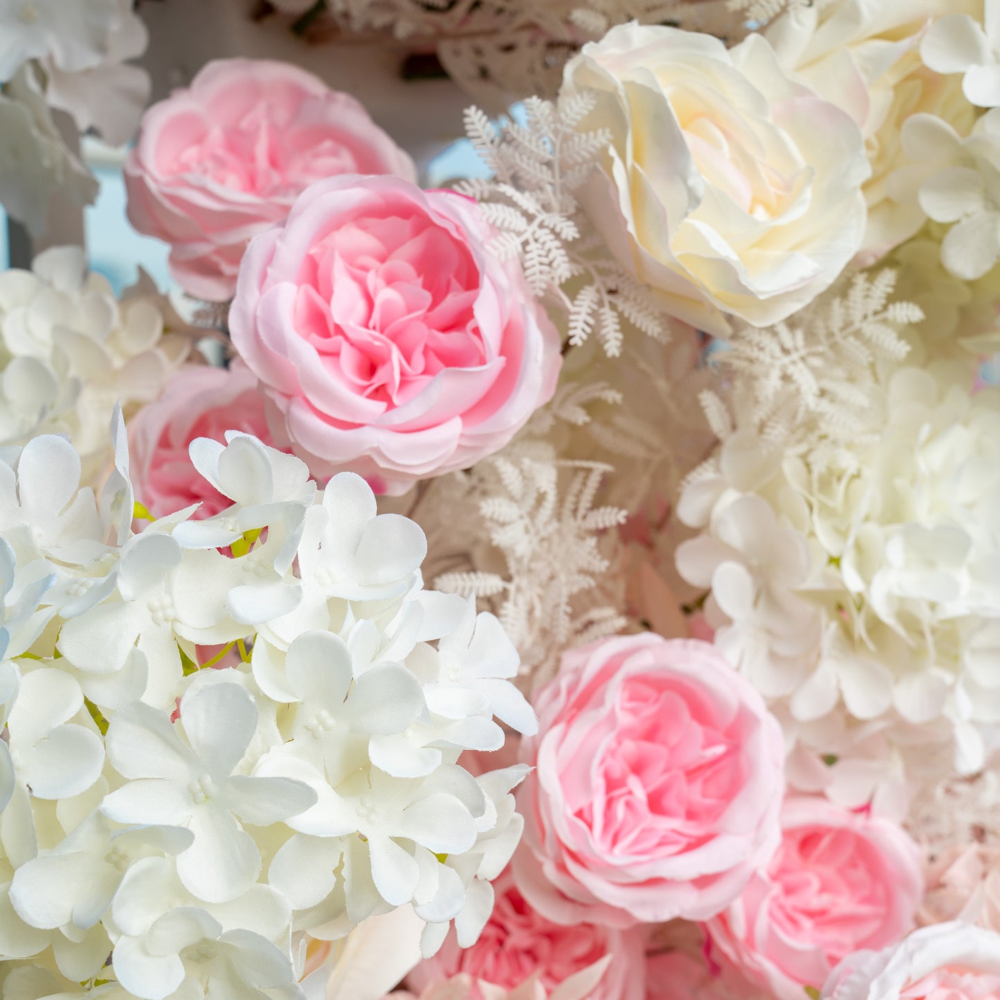 This backdrop features a lush arrangement of artificial flowers. It prominently includes pink and white roses, white hydrangeas, and delicate white fern - like foliage. The color palette is a soft blend of pastel pinks and pure whites, creating a romantic and elegant style, ideal for wedding or bridal events. 