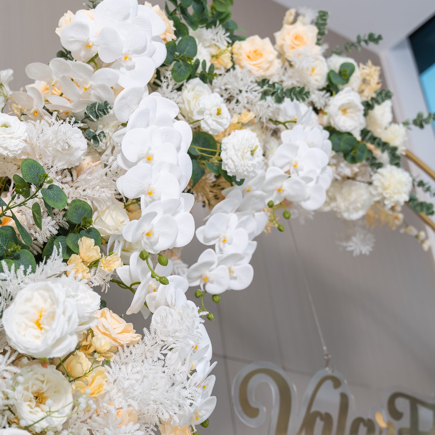 This backdrop features a lush arrangement of artificial flowers. Prominent are white phalaenopsis orchids, accompanied by creamy - hued roses and white chrysanthemums. Green eucalyptus leaves add a touch of nature. The color palette is dominated by whites and soft ivories, creating an elegant and serene style, perfect for refined events. 