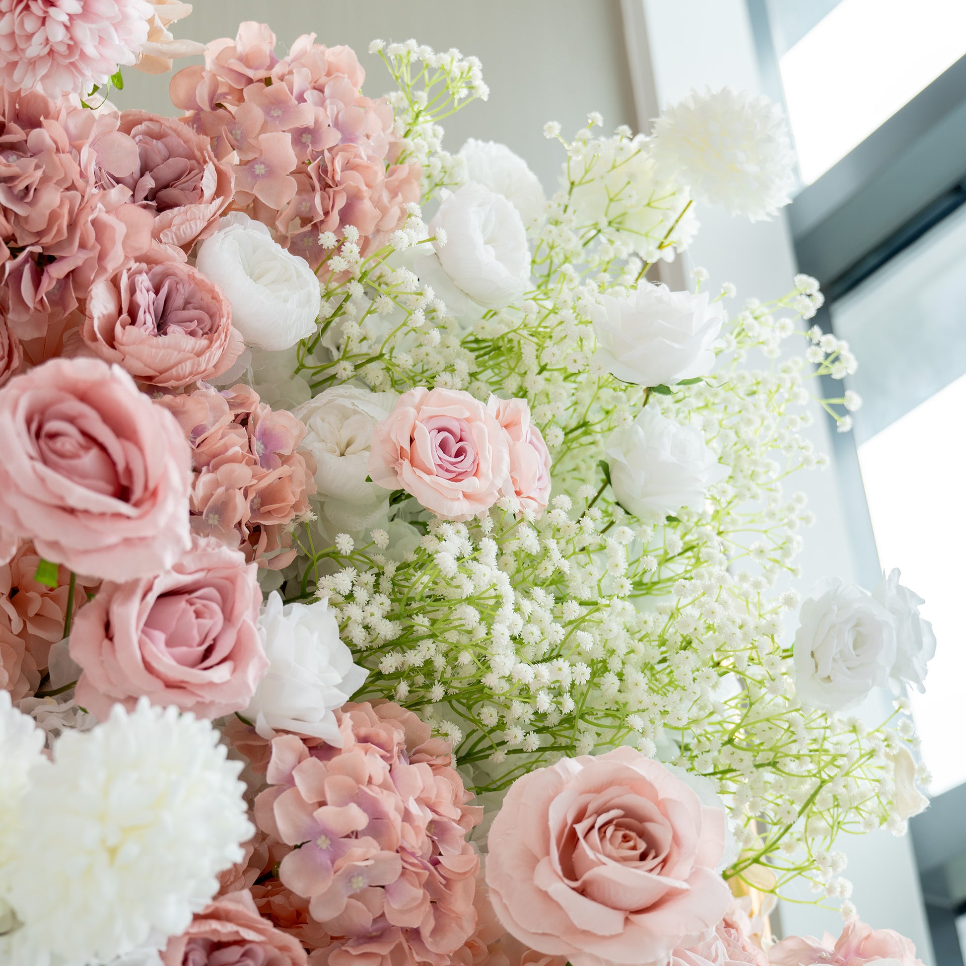 This backdrop showcases a lush arrangement of artificial flowers. It prominently features white and pink roses, white hydrangeas, and clusters of baby's breath. The color palette is a soft blend of whites, light pinks, and hints of green from the foliage. The style is romantic and elegant,  perfect for wedding or bridal - related events. 