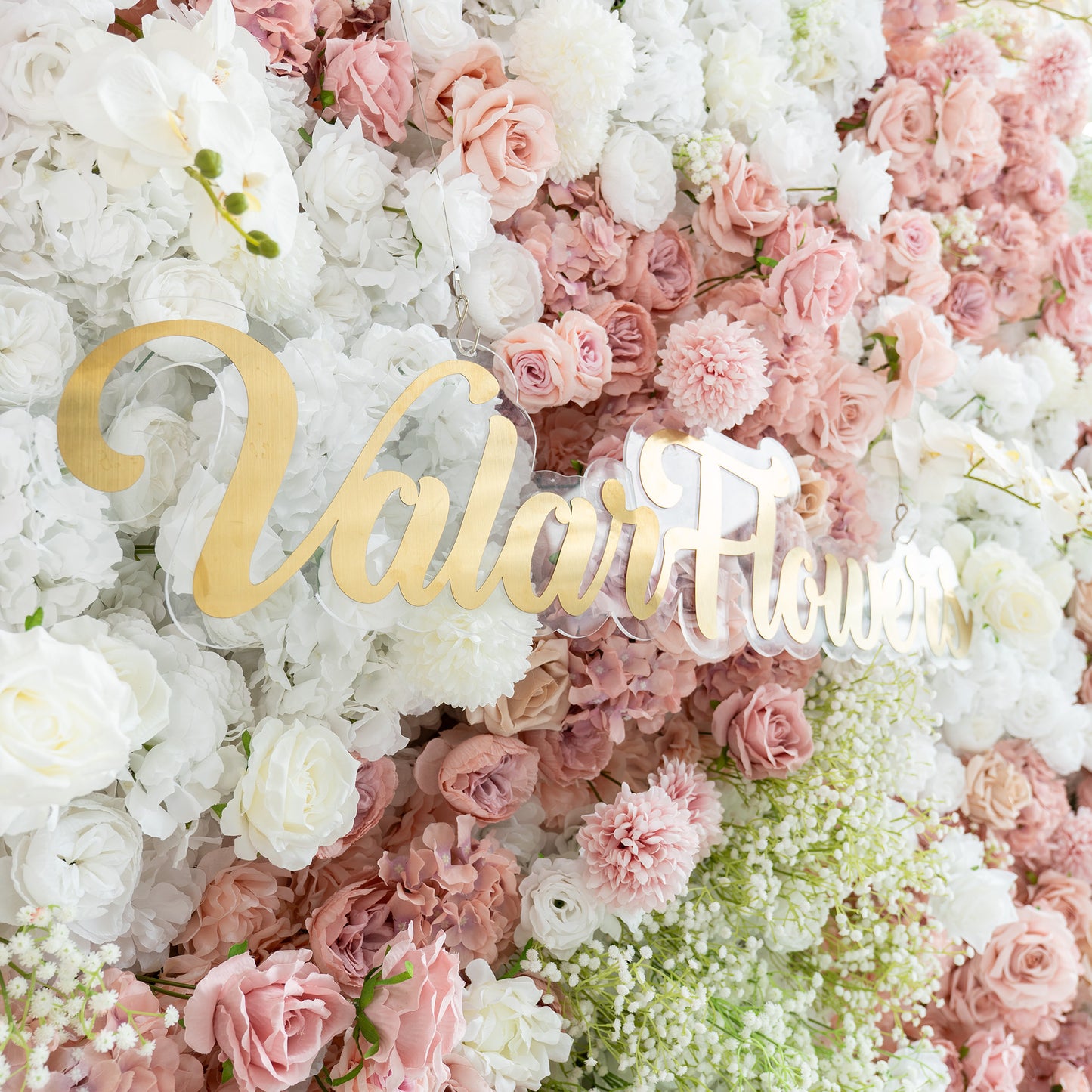 This backdrop features a lush arrangement of artificial flowers. It includes white and pink roses, white hydrangeas, and clusters of baby's breath. The color palette is a soft blend of whites, light pinks, and hints of green. The style is romantic and elegant, perfect for wedding - related events or bridal celebrations. The "ValarFlowers" sign in gold adds a touch of sophistication. 