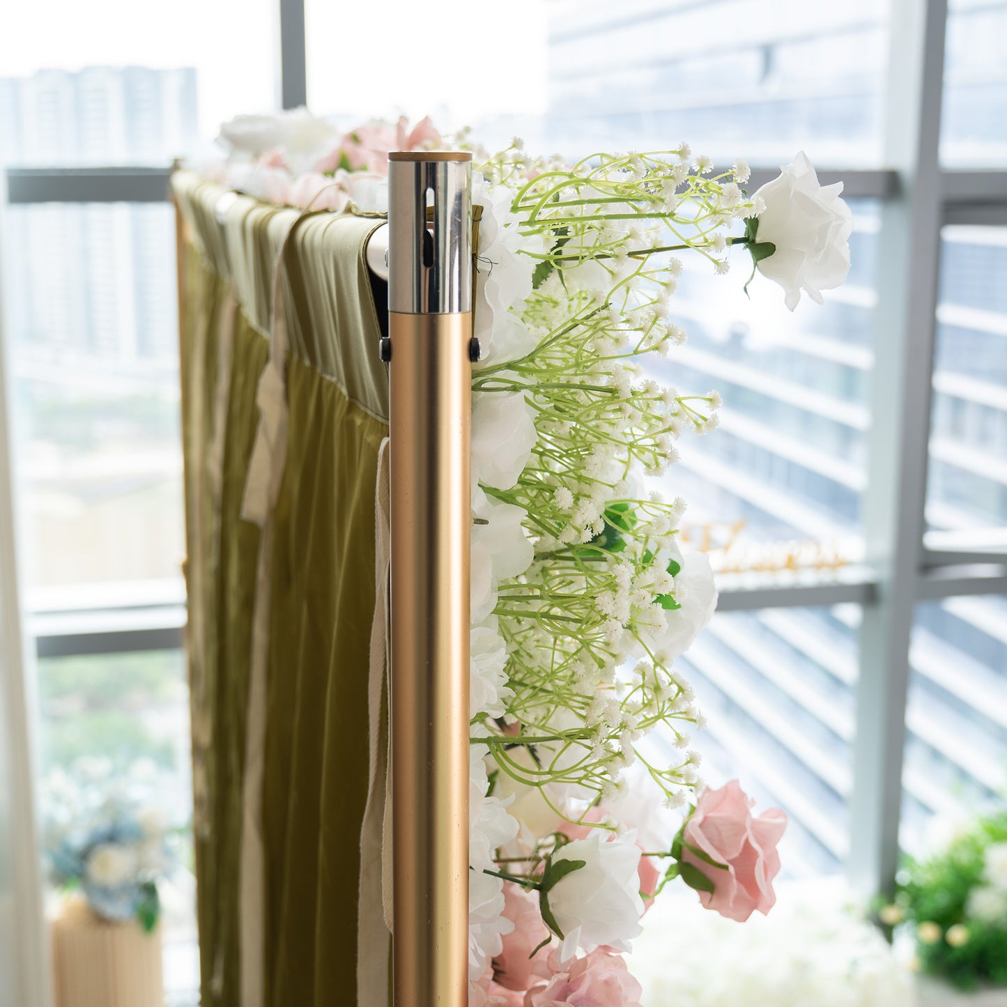 This backdrop features a frame with a metallic finish, partially adorned with artificial flowers. Prominent flowers include white roses and clusters of baby's breath, along with some light - pink roses. The color palette is soft, with whites, light pinks, and green from the foliage. The style is delicate and romantic, suitable for events like weddings or bridal showers. 