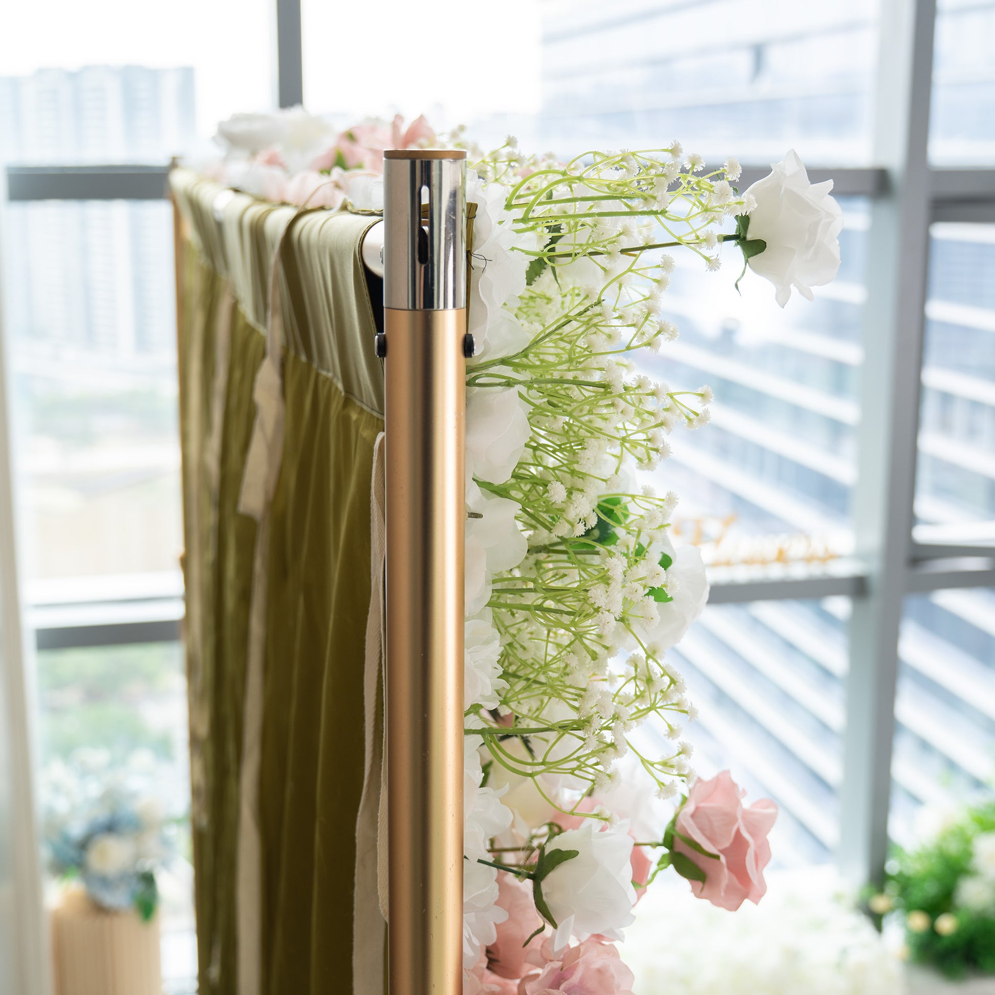 This backdrop features a frame with a metallic finish, partially adorned with artificial flowers. Prominent flowers include white roses and clusters of baby's breath, along with some light - pink roses. The color palette is soft, with whites, light pinks, and green from the foliage. The style is delicate and romantic, suitable for events like weddings or bridal showers. 