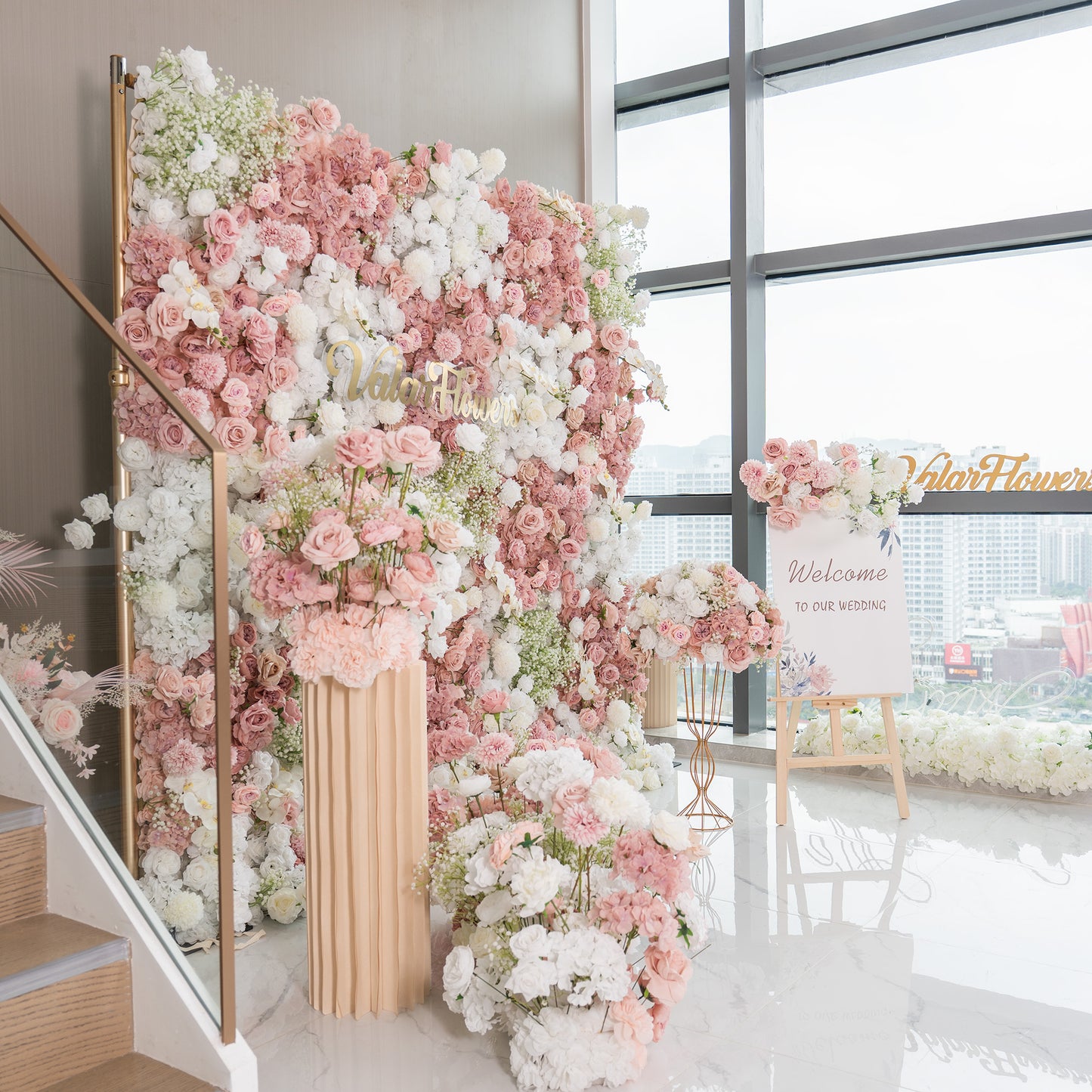 This backdrop is a lush floral wall, perfect for a wedding setting as indicated by the “Welcome to our wedding” sign. It features a mix of artificial roses in soft pinks and whites, along with white hydrangeas and baby's breath. The color palette is pastel - heavy, creating a romantic and elegant style. 