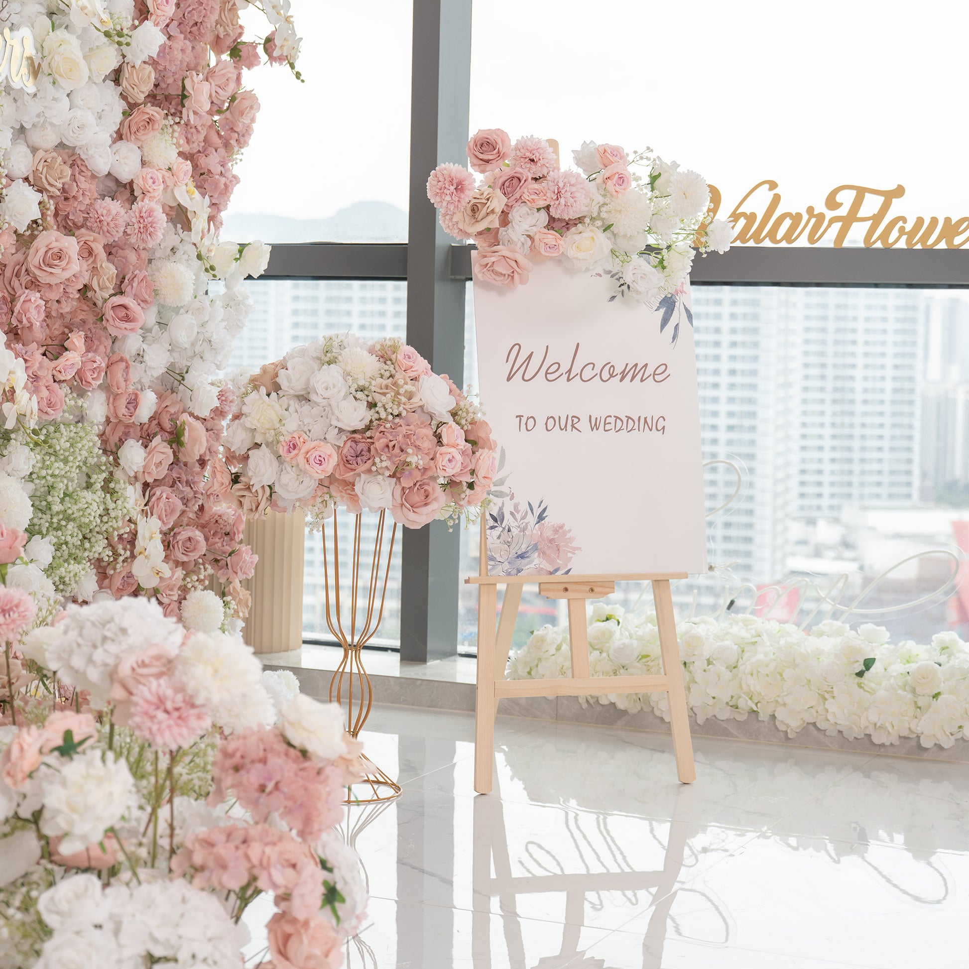 This wedding - themed backdrop features a lush floral wall with artificial flowers. It includes roses in various shades of pink and white, along with white hydrangeas and baby's breath. The color palette is soft and pastel - toned, creating a romantic and elegant style. The “Welcome to our wedding” sign adds a warm greeting to guests. 