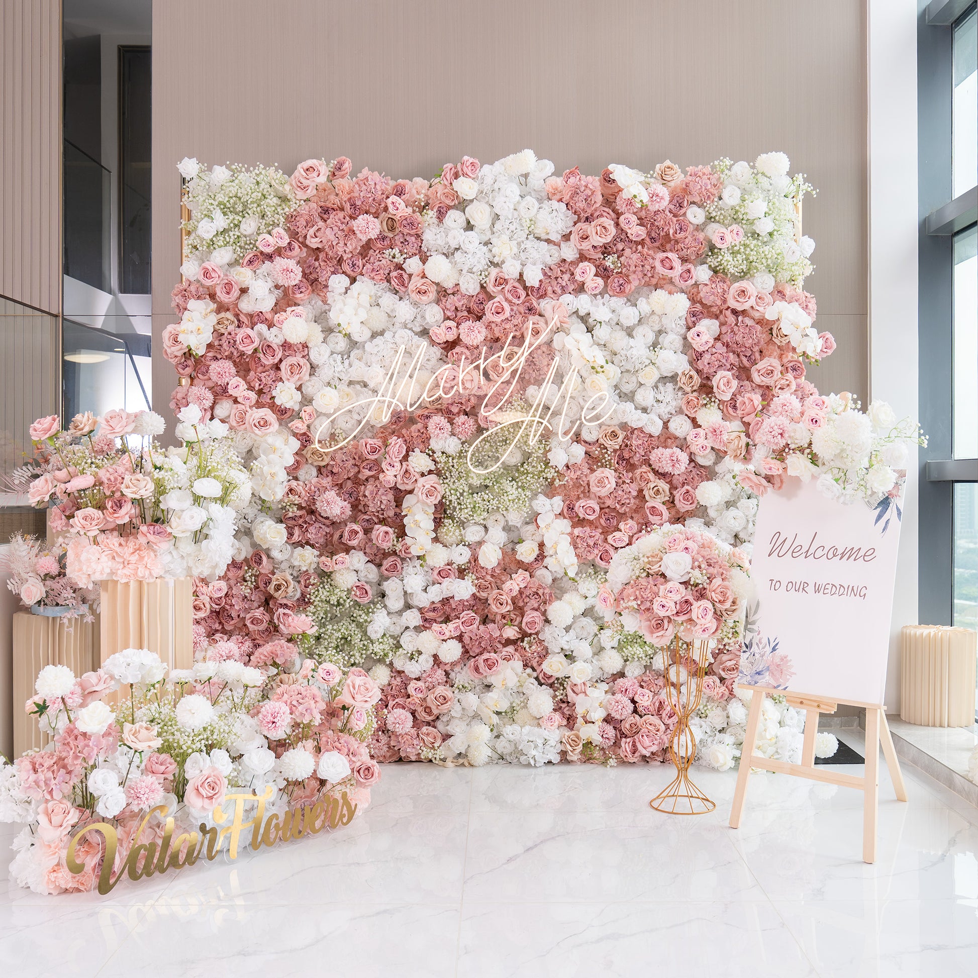 This backdrop is a lush floral arrangement, ideal for a wedding as indicated by the “Welcome to our wedding” sign. It features a mix of artificial roses in shades of pink and white, white chrysanthemums, and clusters of baby's breath. The color palette is soft and pastel - toned, creating a romantic and elegant style. 