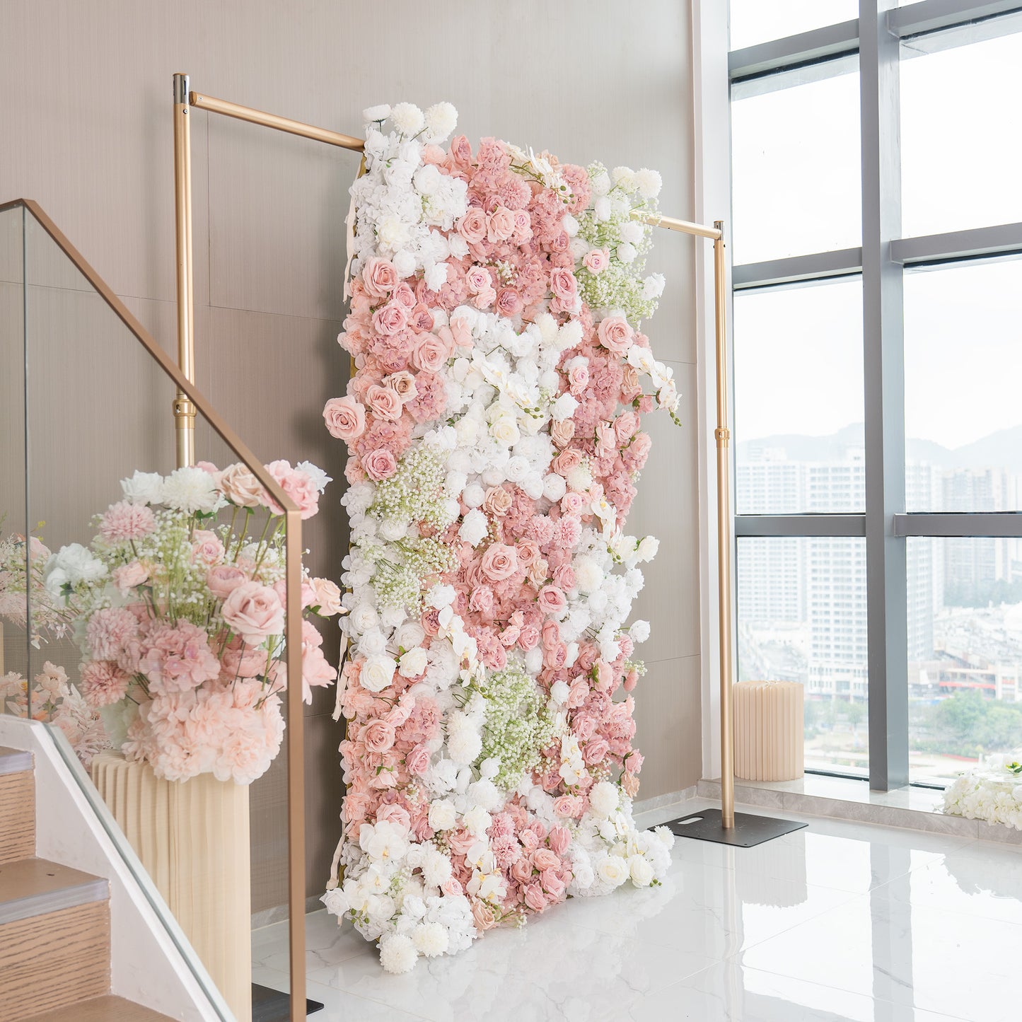 This backdrop is a vertical floral wall supported by golden - hued metal frames. It is densely adorned with artificial flowers, including roses in shades of pink and white, white chrysanthemums, and clusters of baby's breath. The color palette is soft, with pastel pinks and whites, creating a romantic and elegant style, perfect for wedding events. 