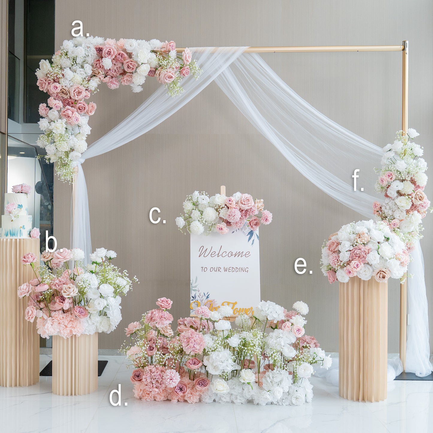 This image showcases a beautifully arranged wedding welcome area. A golden - framed arch adorned with white drapery and clusters of pink and white artificial flowers serves as the centerpiece. Below it, a sign reading "Welcome to our wedding" is surrounded by more floral arrangements in soft hues. The setup includes tall, pleated vases filled with flowers, creating an elegant and romantic atmosphere. 