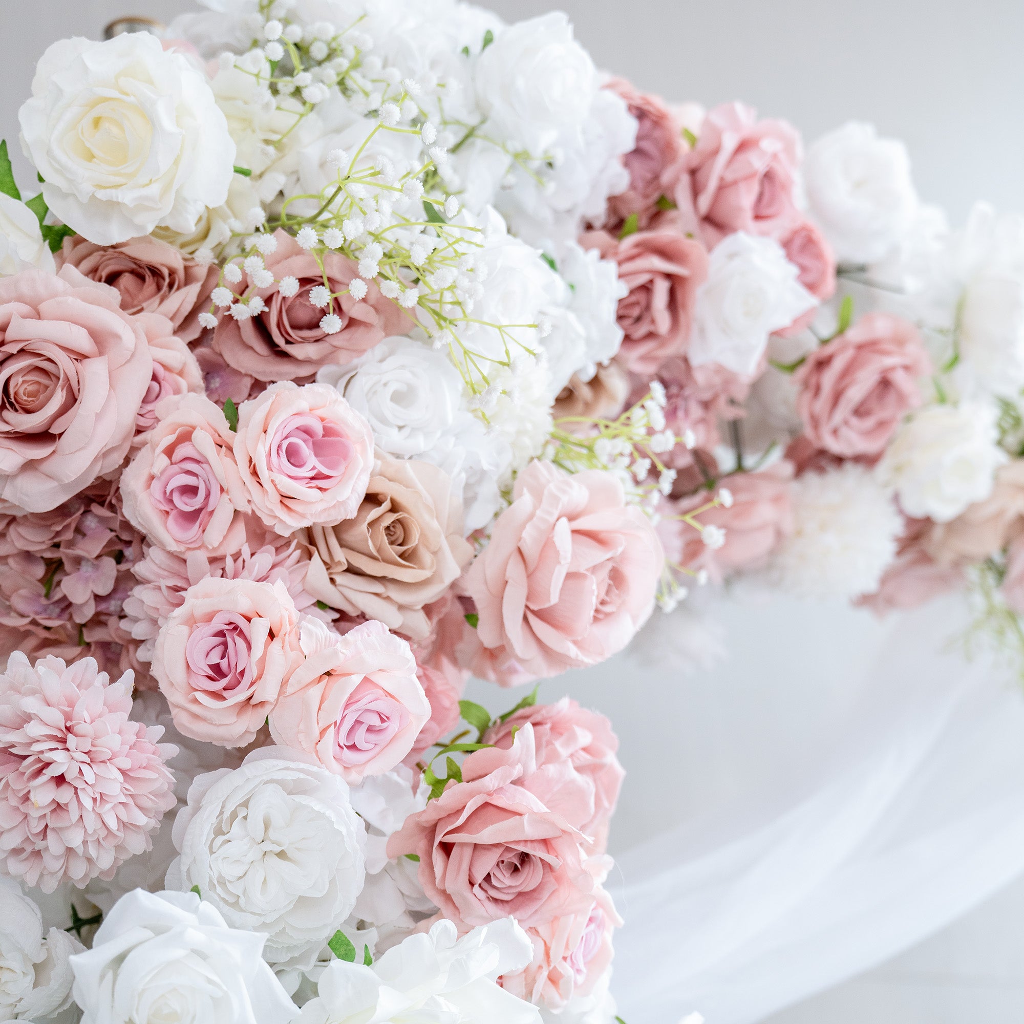This image showcases a lush arrangement of artificial flowers in soft, romantic hues. Prominent are roses in shades of white, light pink, and blush, interspersed with delicate white baby&
