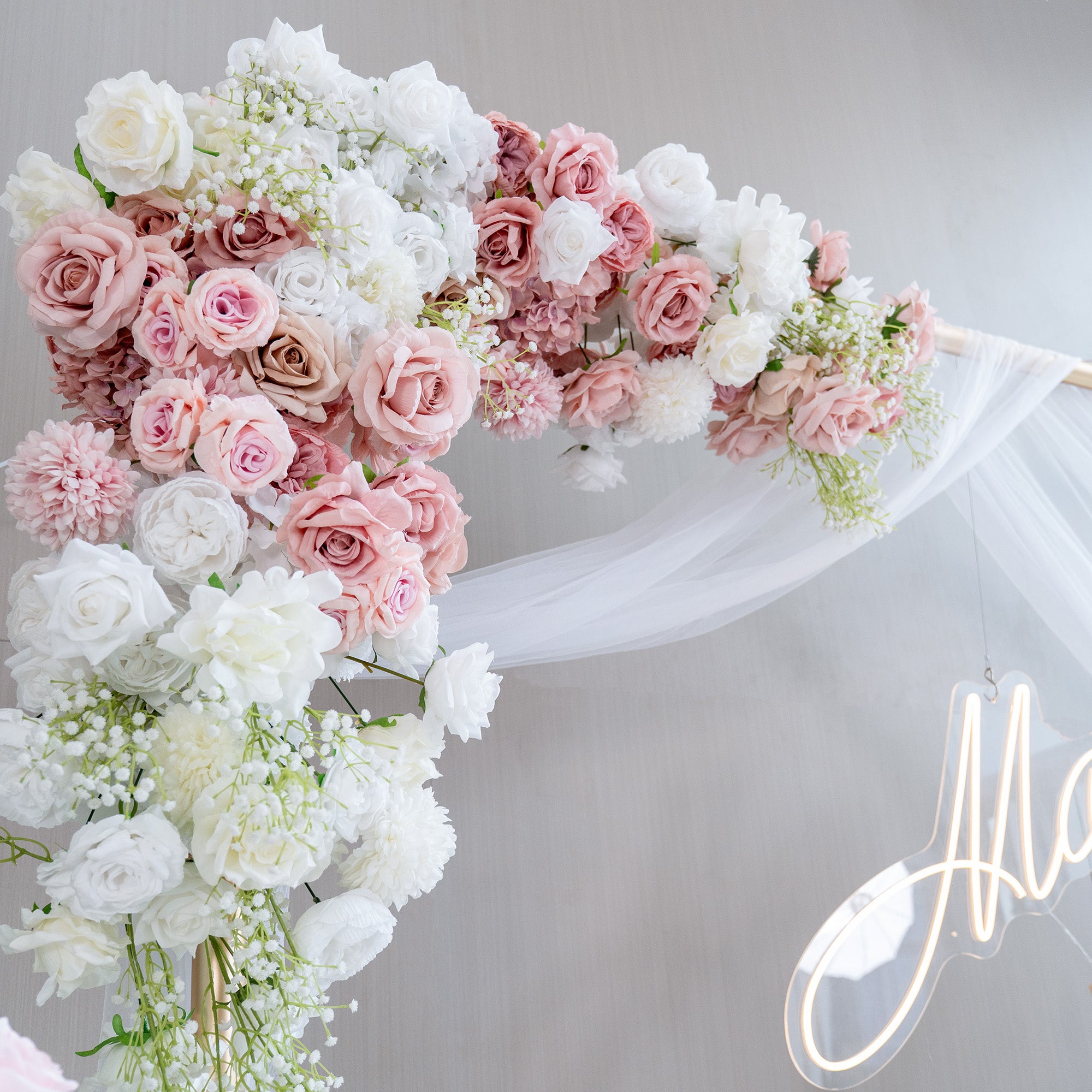 This image features a stunning floral arrangement on an archway, likely for a wedding or special event. The flowers include roses in shades of white, blush pink, and light peach, interspersed with delicate white baby&