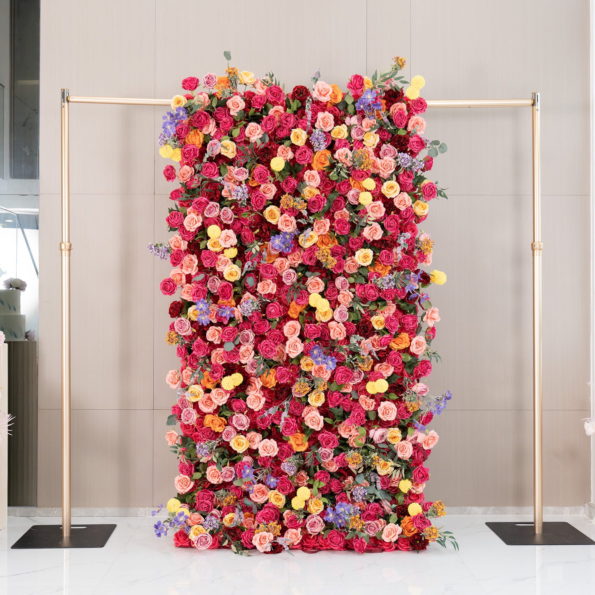 This image features a lush floral wall supported by a metallic gold frame. The wall is densely adorned with artificial flowers, mainly roses in rich shades of red, pink, and peach, along with bright yellow pom - pom flowers and delicate purple blooms. The style is vibrant and romantic, perfect for special events. 