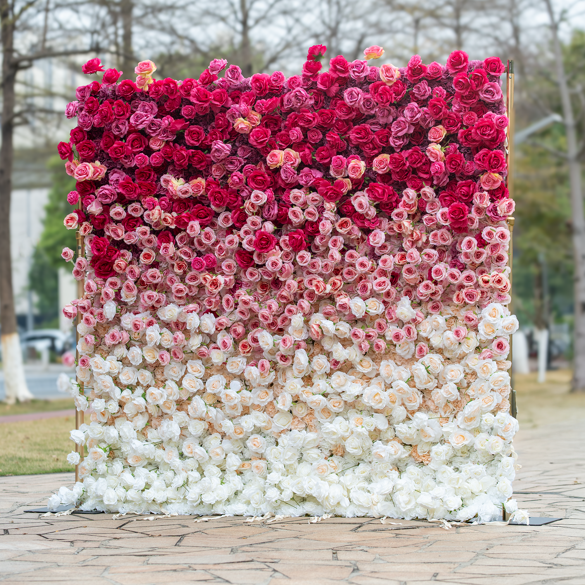 This backdrop features a dense arrangement of artificial roses in a striking gradient, transitioning from deep red at the top to soft white at the bottom. Set against an outdoor park - like backdrop, it creates a romantic and luxurious atmosphere, perfect for weddings or events. 