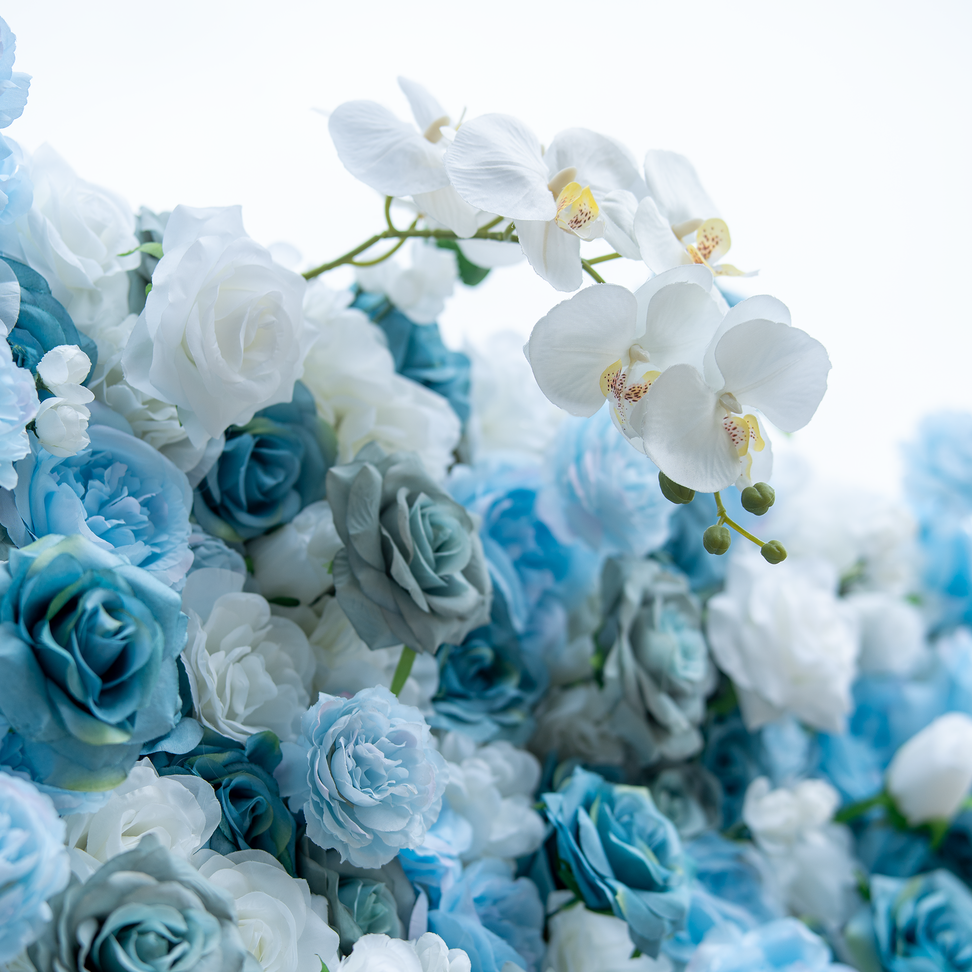This photo showcases a lush floral arrangement with a harmonious blend of blue and white roses, complemented by elegant white orchids. The soft hues create a serene and sophisticated atmosphere. The dense clustering of flowers highlights their texture and depth, with the orchids' delicate petals and prominent yellow centers adding a touch of refinement. Ideal for upscale events like weddings or galas, it exudes an air of grace and beauty. 