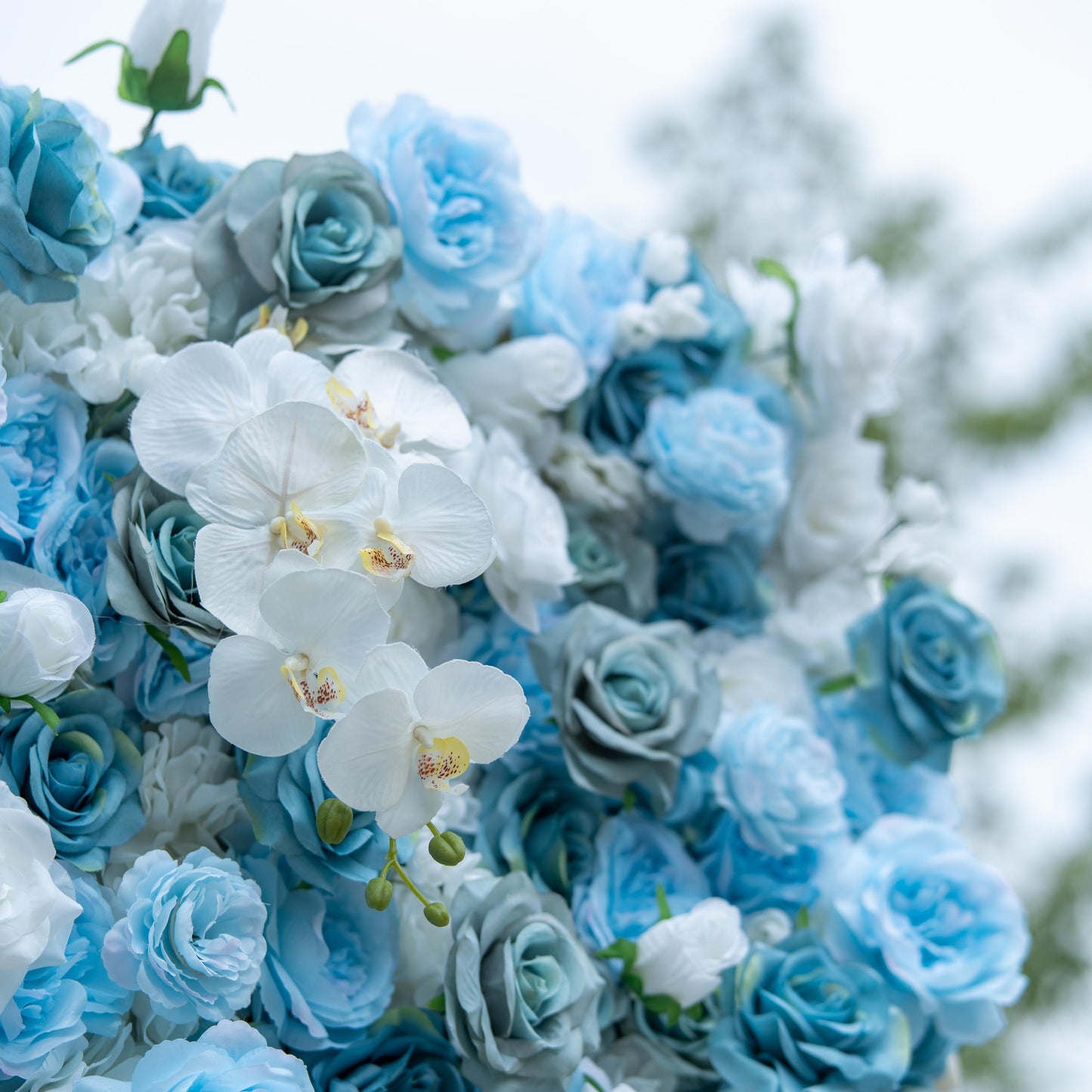 This photo showcases a lush, vibrant floral arrangement featuring a blend of blue and white roses interspersed with white orchids. The delicate white orchids, with their prominent yellow centers, stand out against the soft - hued roses. The varying shades of blue and white create a harmonious and calming effect. Ideal for elegant events like weddings or upscale galas, this arrangement exudes sophistication and beauty. 