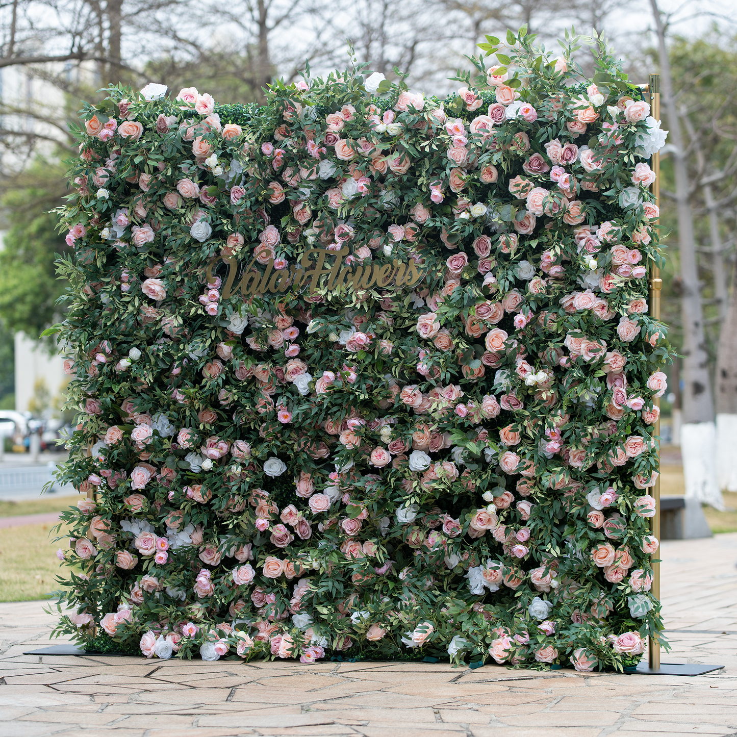 This photo showcases a large floral backdrop brimming with pink and white roses, interspersed with lush green foliage. In the center, golden lettering reads "ValarFlowers". Ideal for events like bridal showers or garden - themed corporate functions, it fits a "Romantic Garden Soirée" theme. The soft hues and dense arrangement exude elegance and charm, making it a perfect decorative piece. 