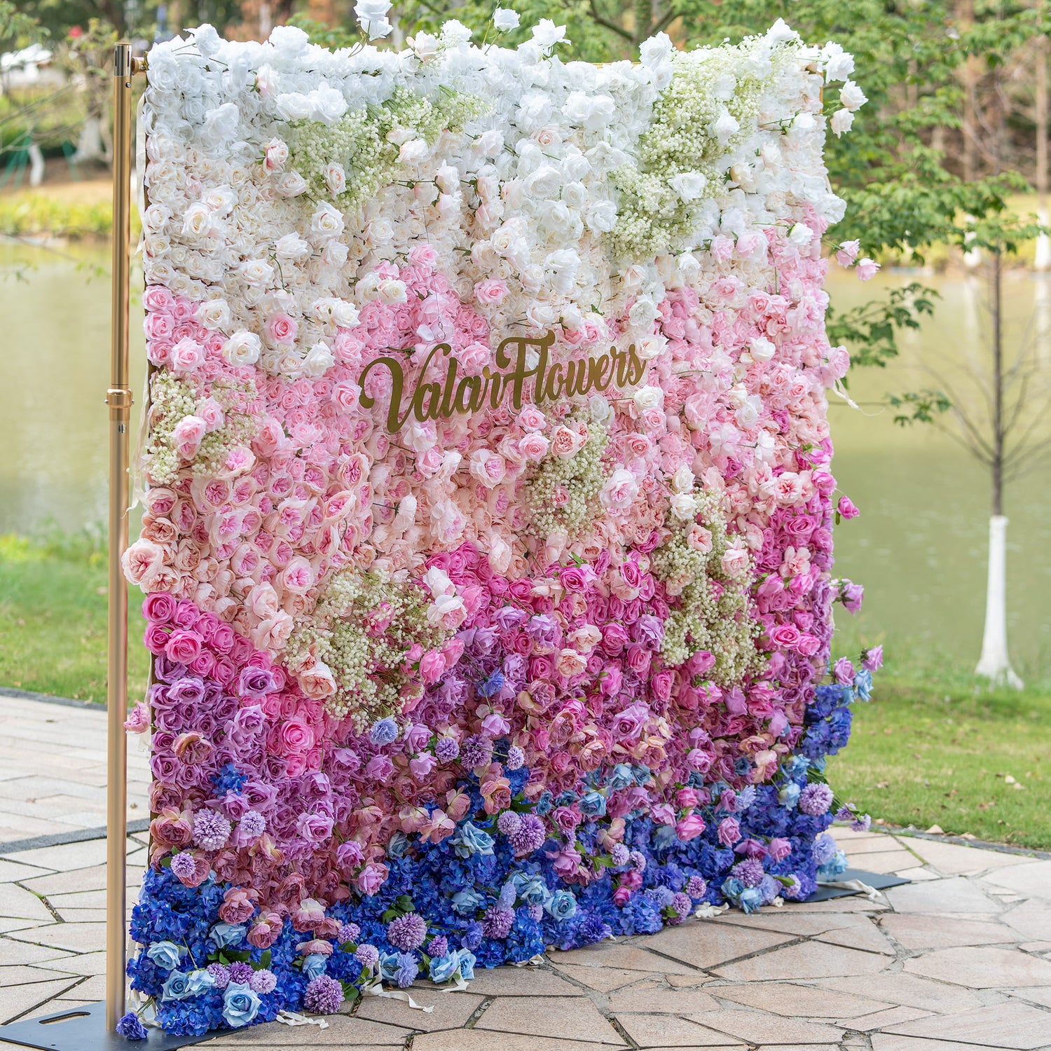 This photo displays a vibrant floral wall with a gradient of white, pink, and blue. Composed mainly of roses and hydrangeas, with baby&