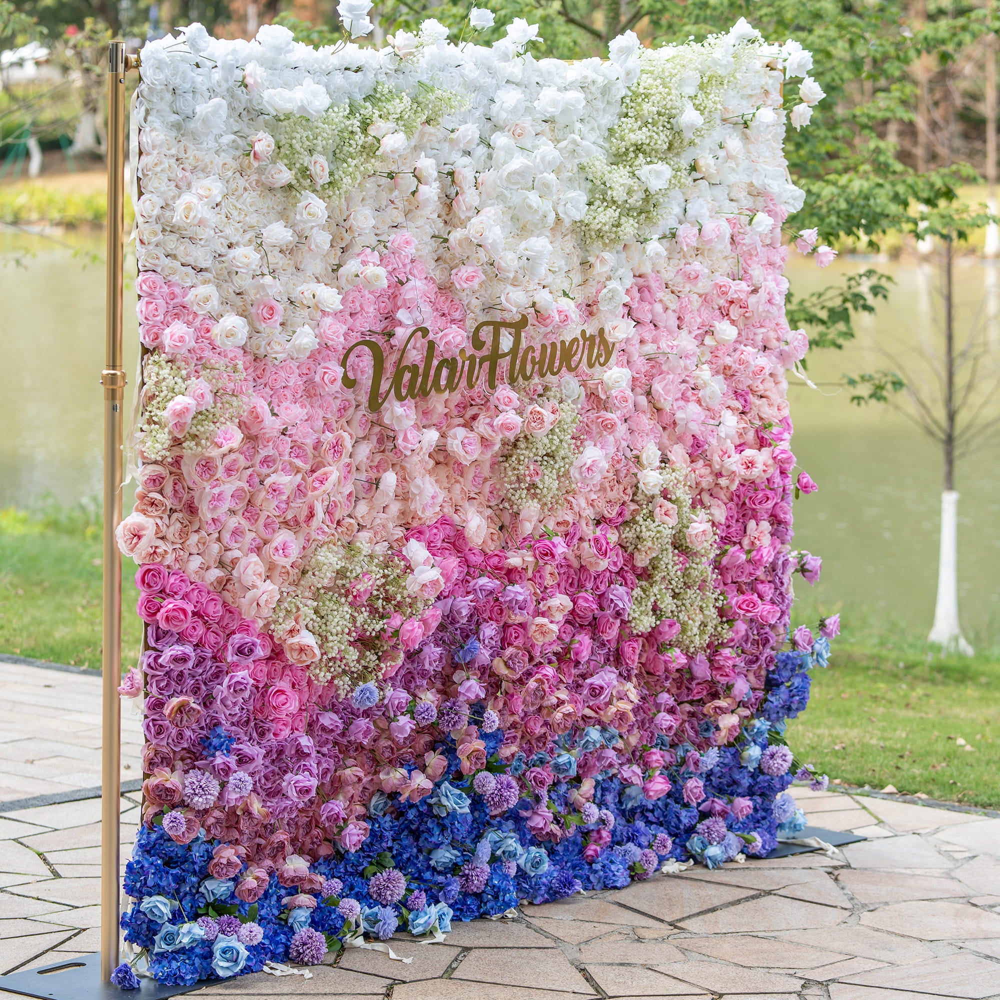 This photo displays a vibrant floral wall with a gradient of white, pink, and blue. Composed mainly of roses and hydrangeas, with baby&