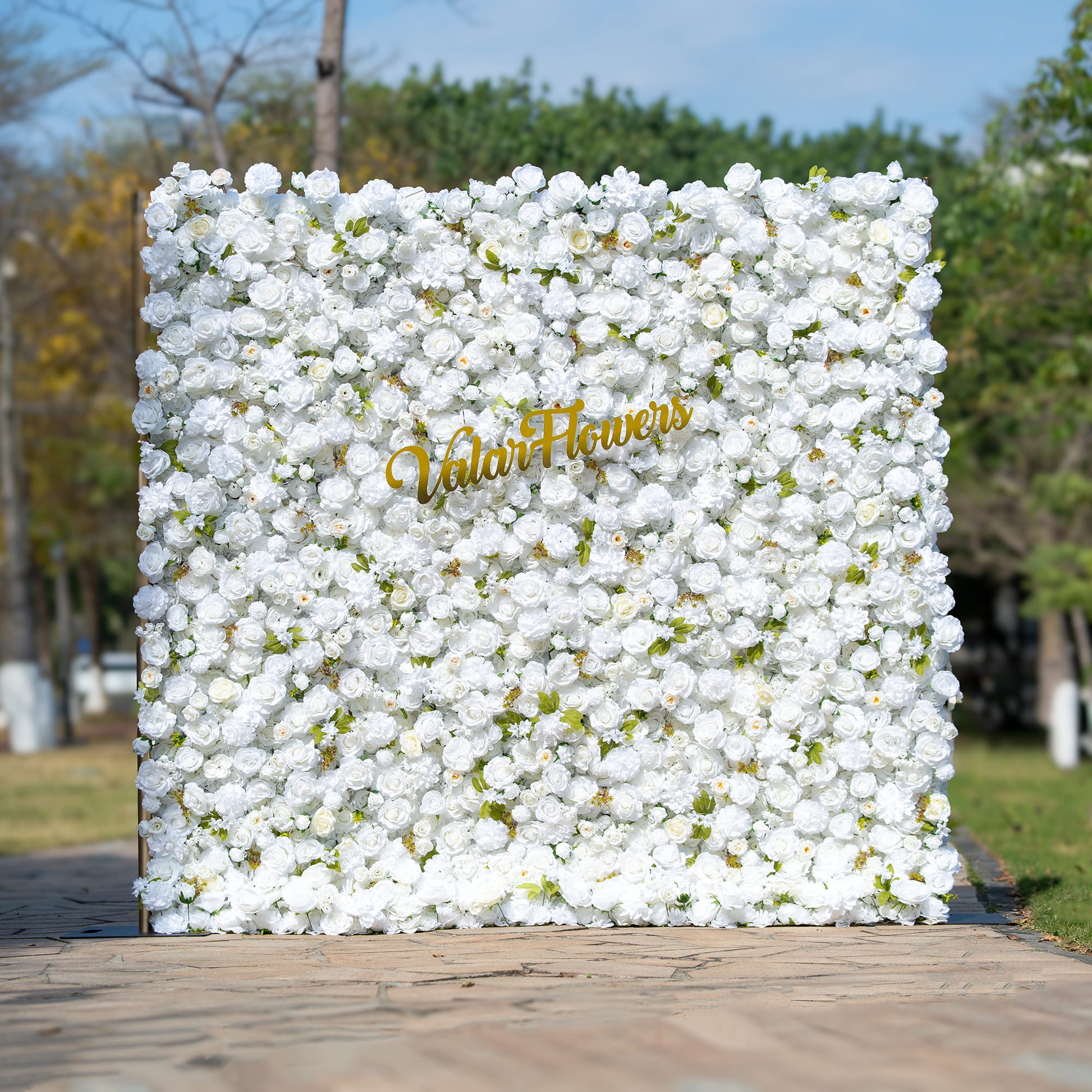 This floral backdrop is densely covered with artificial white roses, interspersed with small green leaves, creating a clean and pure look. The all - white color palette exudes a sense of elegance and simplicity. The golden “ValarFlowers” sign adds a touch of luxury. The overall style is classic and sophisticated, suitable for formal events like weddings or corporate functions. 