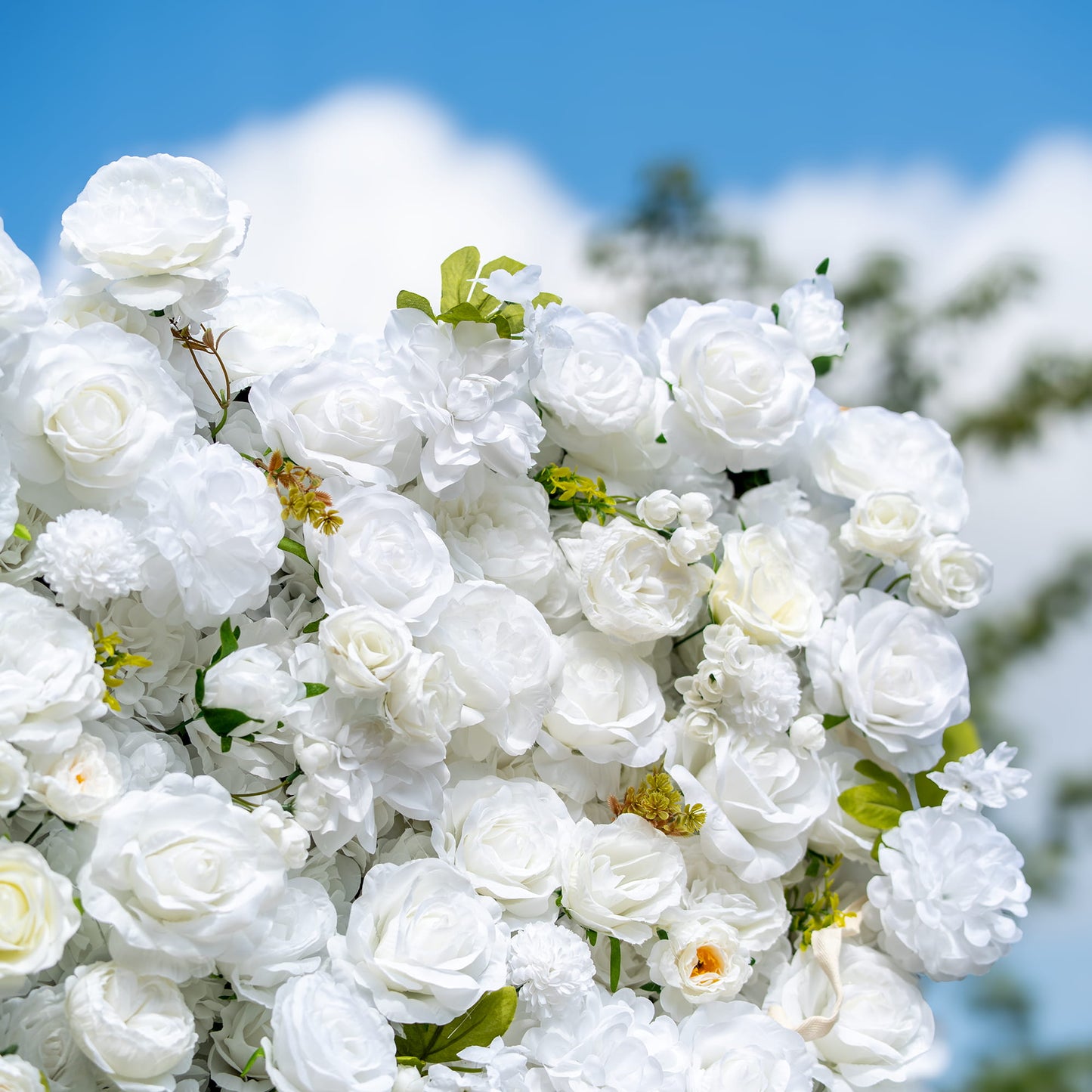 This close - up image showcases a lush arrangement of artificial white flowers, predominantly roses, along with some peony - like blooms and small, round blossoms. Interspersed with green leaves, the color palette is a pure white accented by green. The style is elegant and pristine, exuding a sense of purity and sophistication, ideal for formal events. 