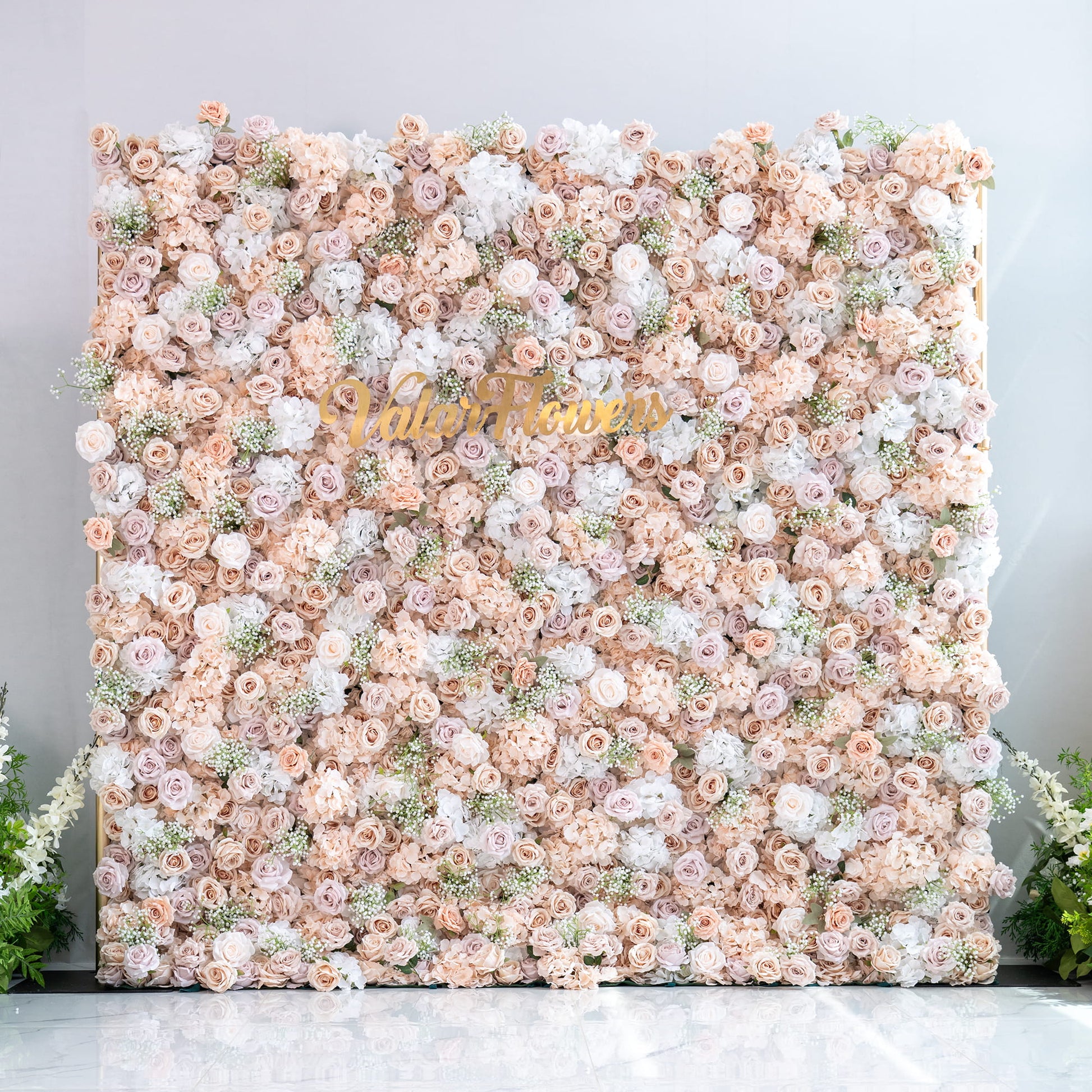 This floral backdrop is a lush, full - coverage arrangement. It features a mix of artificial roses in various shades of blush, beige, and white, interspersed with clusters of baby's breath. The color palette is soft and neutral, creating a warm and elegant style, perfect for wedding or event photo booths. The “ValarFlowers” sign adds a branding touch. 