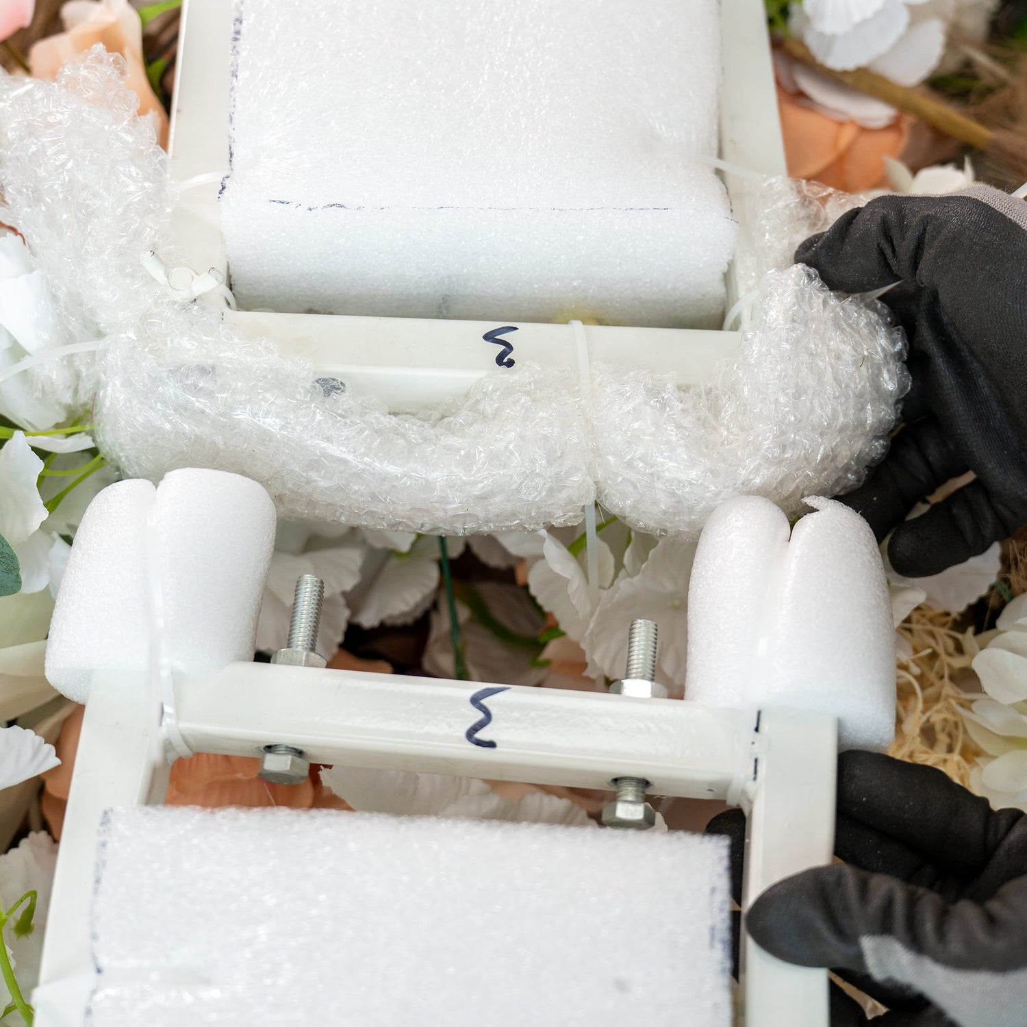 This image actually shows a close - up of a structure with protective materials rather than a backdrop. There are white foam rollers and bubble wrap, along with metal bolts and nuts. Gloved hands are interacting with the components. It seems to be part of a setup or disassembly process, but there is no backdrop visible in the traditional sense. 