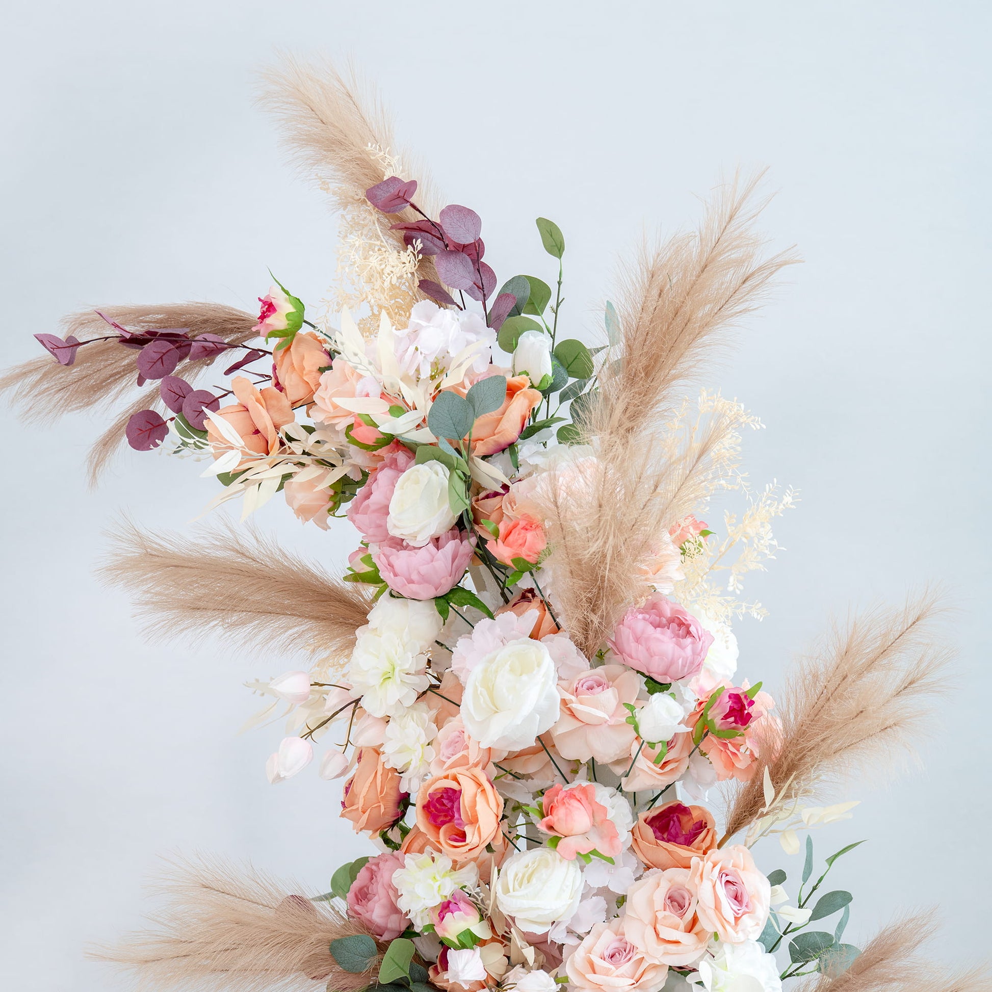This backdrop showcases a lush floral arrangement with a mix of flowers. There are roses in shades of pink, peach, and white, along with peonies. Eucalyptus and other greenery add a fresh touch, while pampas grass provides a soft, neutral contrast.

The color palette features soft pastels like pink, peach, and white, complemented by green foliage and beige - toned pampas grass. The style is romantic and elegant, perfect for a wedding or a sophisticated event. 