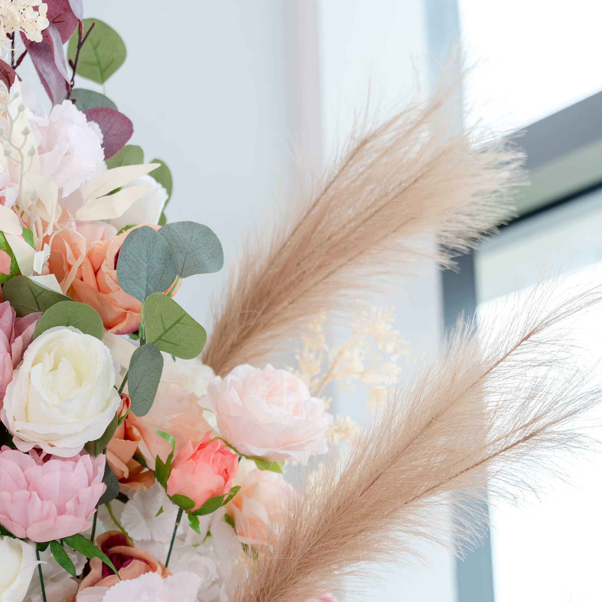 This backdrop features a lush arrangement of artificial flowers and foliage. It includes roses in shades of white, pink, and peach, along with peonies and eucalyptus leaves. Pampas - like feathers add a soft, elegant touch. The color palette is soft and pastel - toned, creating a romantic and inviting atmosphere. 
