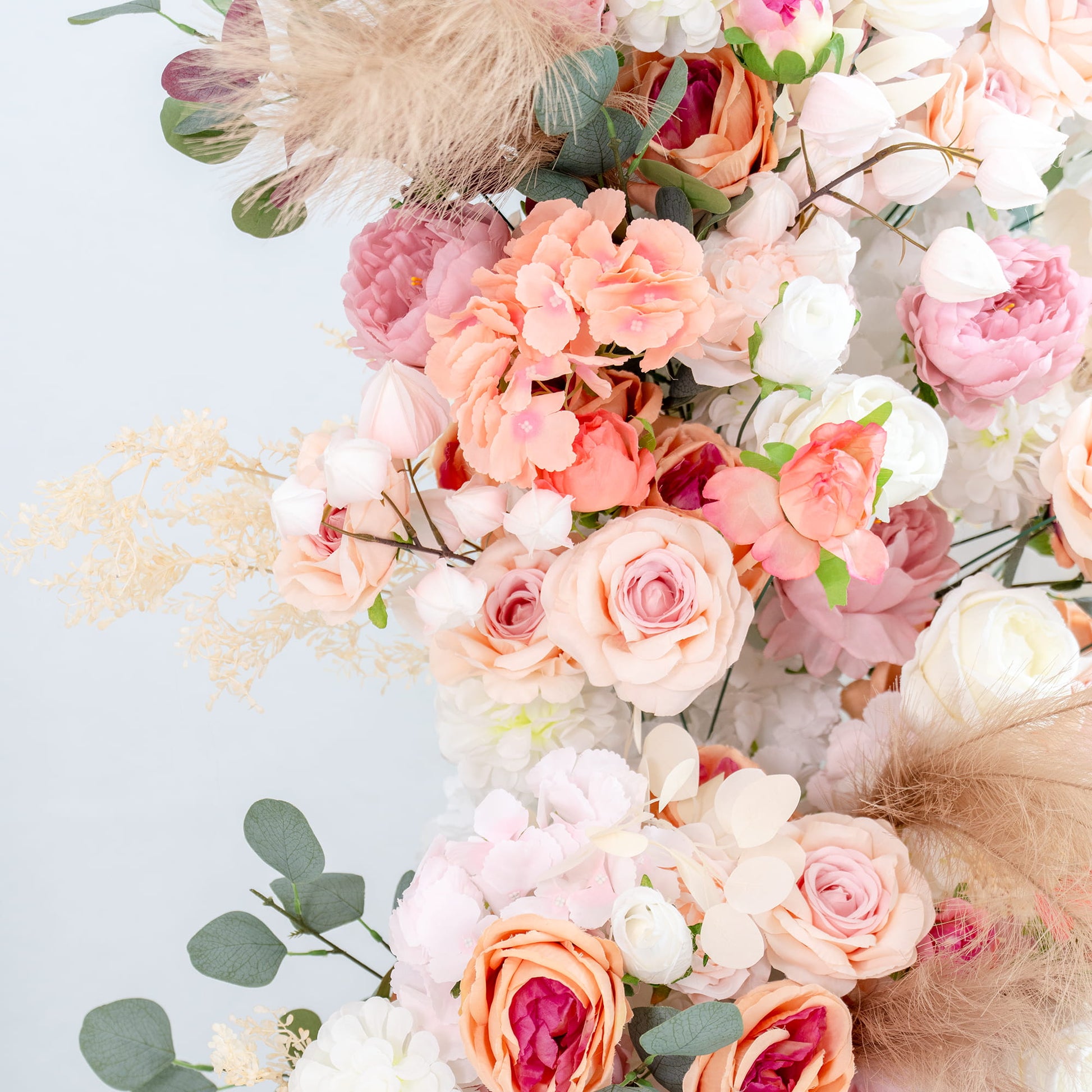 This backdrop features a lush arrangement of artificial flowers in soft, pastel hues. It includes roses in shades of pink, peach, and white, along with peonies and hydrangea - like blooms. Eucalyptus leaves and pampas - like feathers add texture. The overall look is romantic and elegant, perfect for a wedding or a special event. 