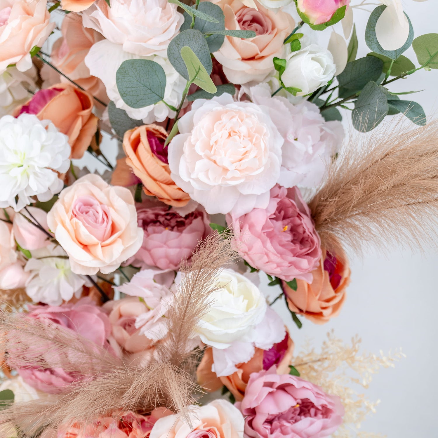 This backdrop features a rich arrangement of artificial flowers in soft pastel tones. There are roses in shades of pink, peach, and white, complemented by peonies. Eucalyptus leaves add a touch of green, while pampas - like feathers lend a soft, airy texture. The overall style is romantic and elegant, perfect for a wedding or a special event. 
