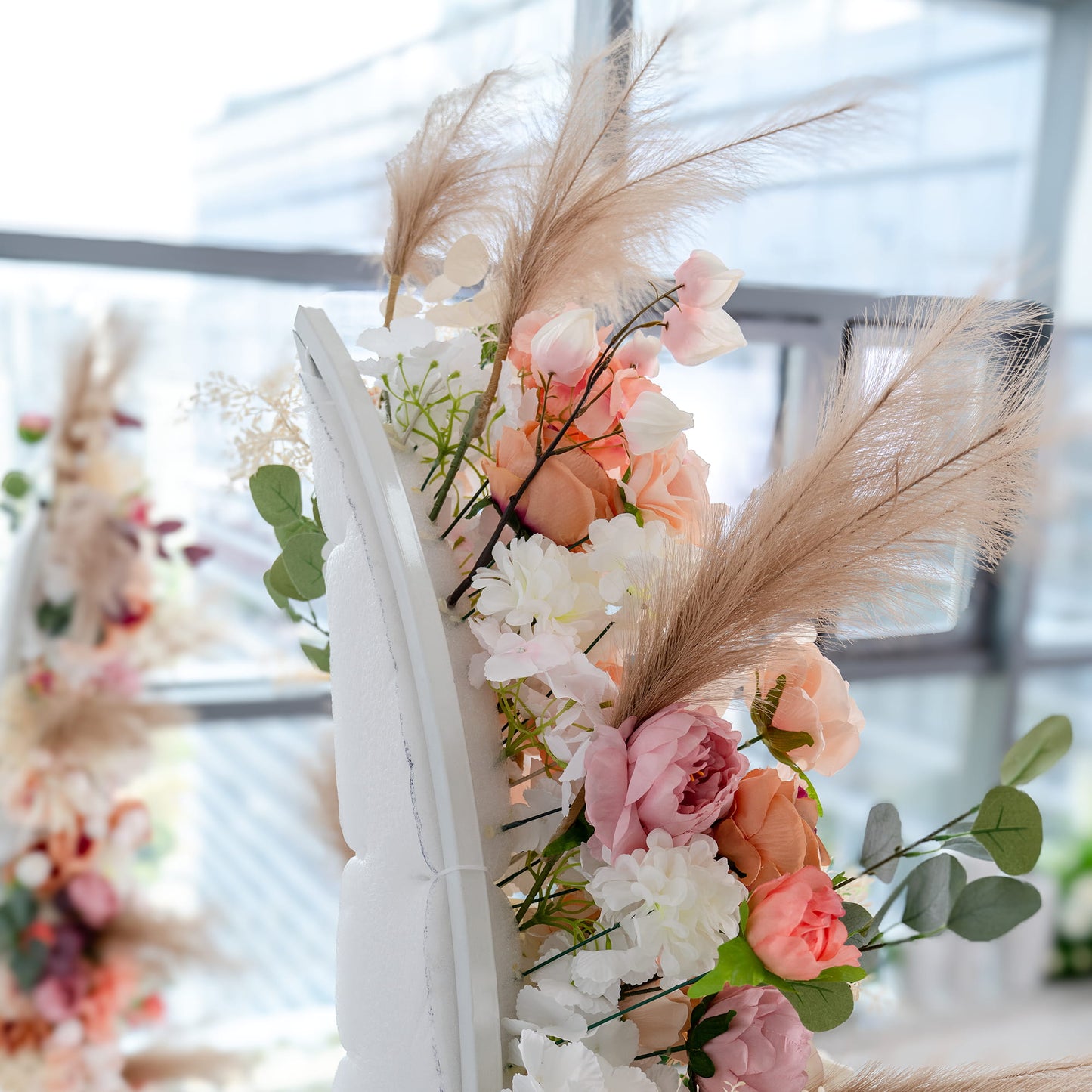 This backdrop showcases a delicate floral arrangement with an array of artificial flowers in soft pastel colors, including pink, peach, and white roses, and peonies. Interspersed with eucalyptus leaves and pampas - like feathers, it exudes a romantic and elegant style, perfect for a wedding or event. 