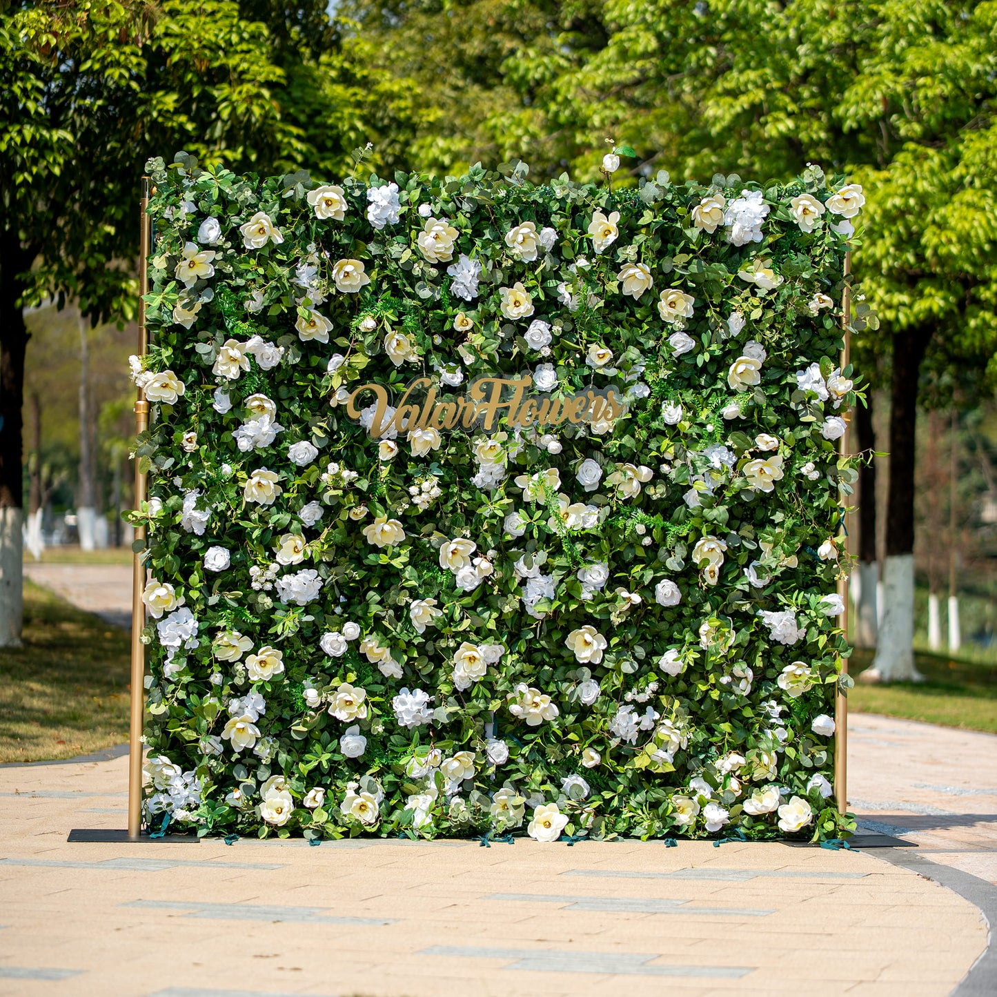 This backdrop features a lush arrangement of artificial green foliage interspersed with white flowers, including roses and camellia - like blooms. The color scheme is a fresh combination of vibrant green and pure white.

The golden - hued "Valar Flowers" sign adds an elegant touch. The overall style is natural and sophisticated, making it suitable for various events such as weddings, corporate functions, or garden parties. 