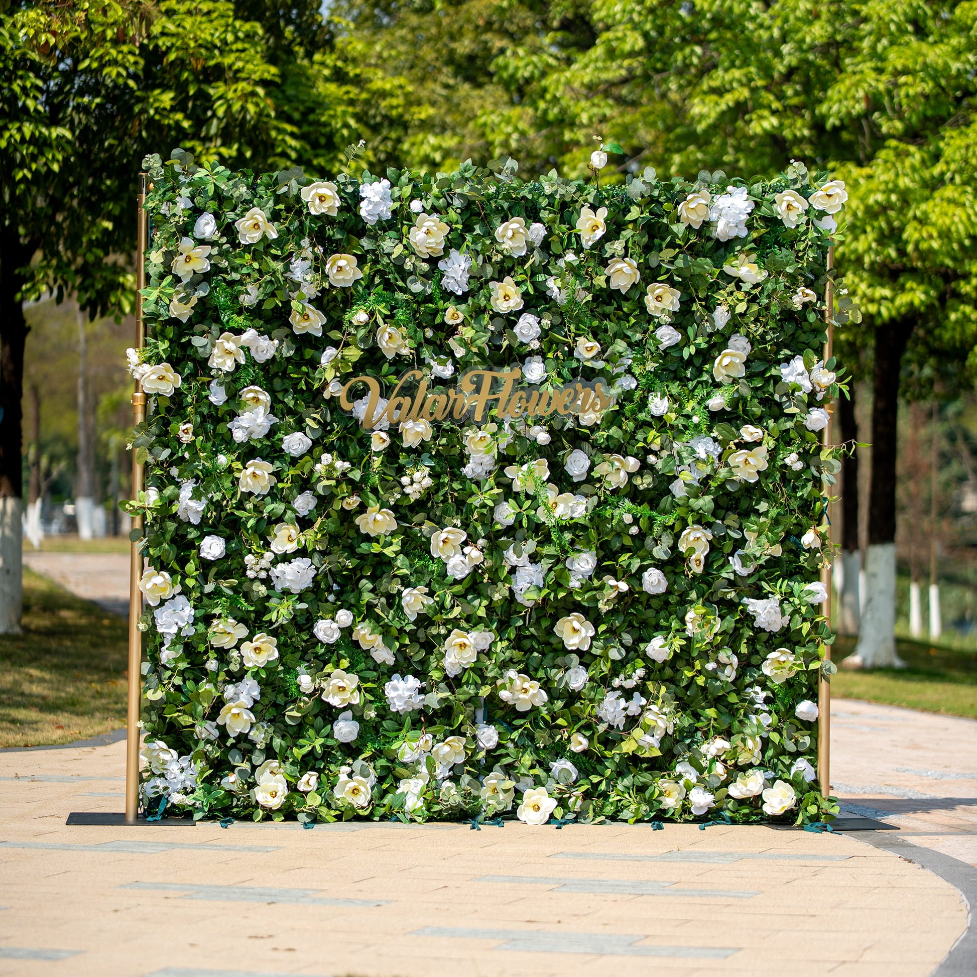 This backdrop features a lush arrangement of artificial green foliage interspersed with white flowers, including roses and camellia - like blooms. The color scheme is a fresh combination of vibrant green and pure white.

The golden - hued "Valar Flowers" sign adds an elegant touch. The overall style is natural and sophisticated, making it suitable for various events such as weddings, corporate functions, or garden parties. 