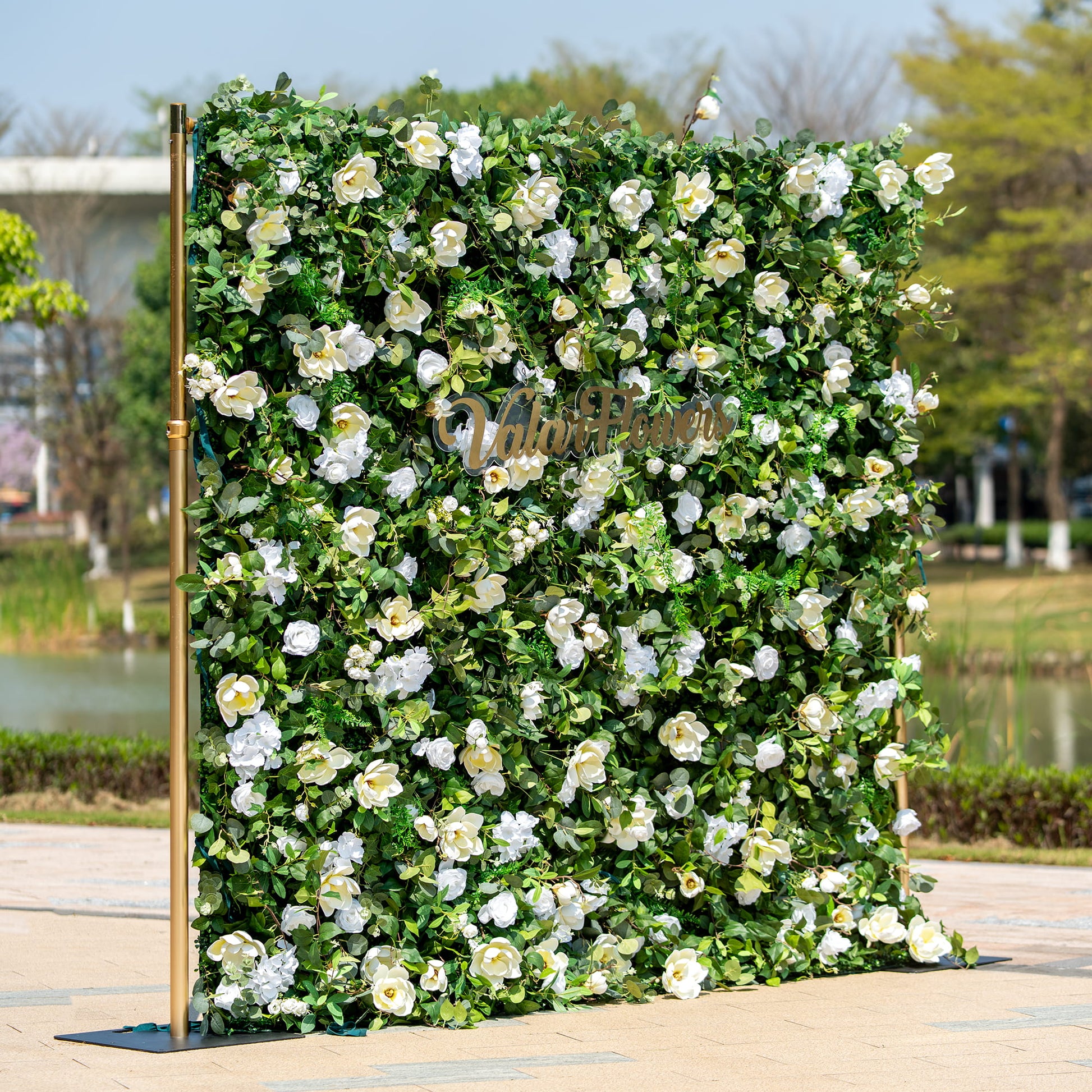 This backdrop is a verdant floral wall supported by golden - hued poles. It is densely packed with artificial green foliage interspersed with white roses and other white blooms. The "Valar Flowers" sign in elegant script adds a touch of sophistication.

The color scheme features a striking contrast between the lush green leaves and the pure white flowers, creating a fresh and natural style. Ideal for events like weddings, corporate gatherings, or garden - themed parties. 