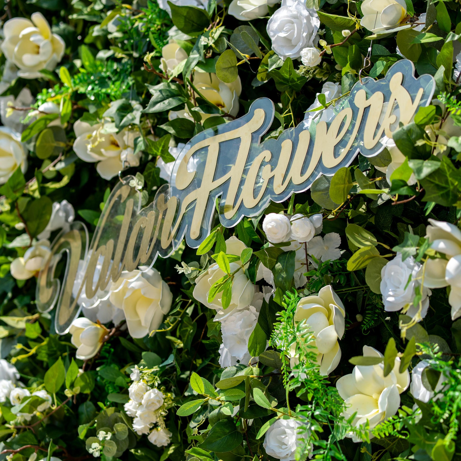 This backdrop is a lush floral wall with a mix of white and cream - colored artificial flowers, including magnolia - like blooms and white roses. The greenery is a dense array of various artificial leaves, creating a rich, verdant base. This backdrop features artificial white magnolias, roses, and hydrangeas among lush green foliage. Colors are white and green, with a natural, elegant style. 