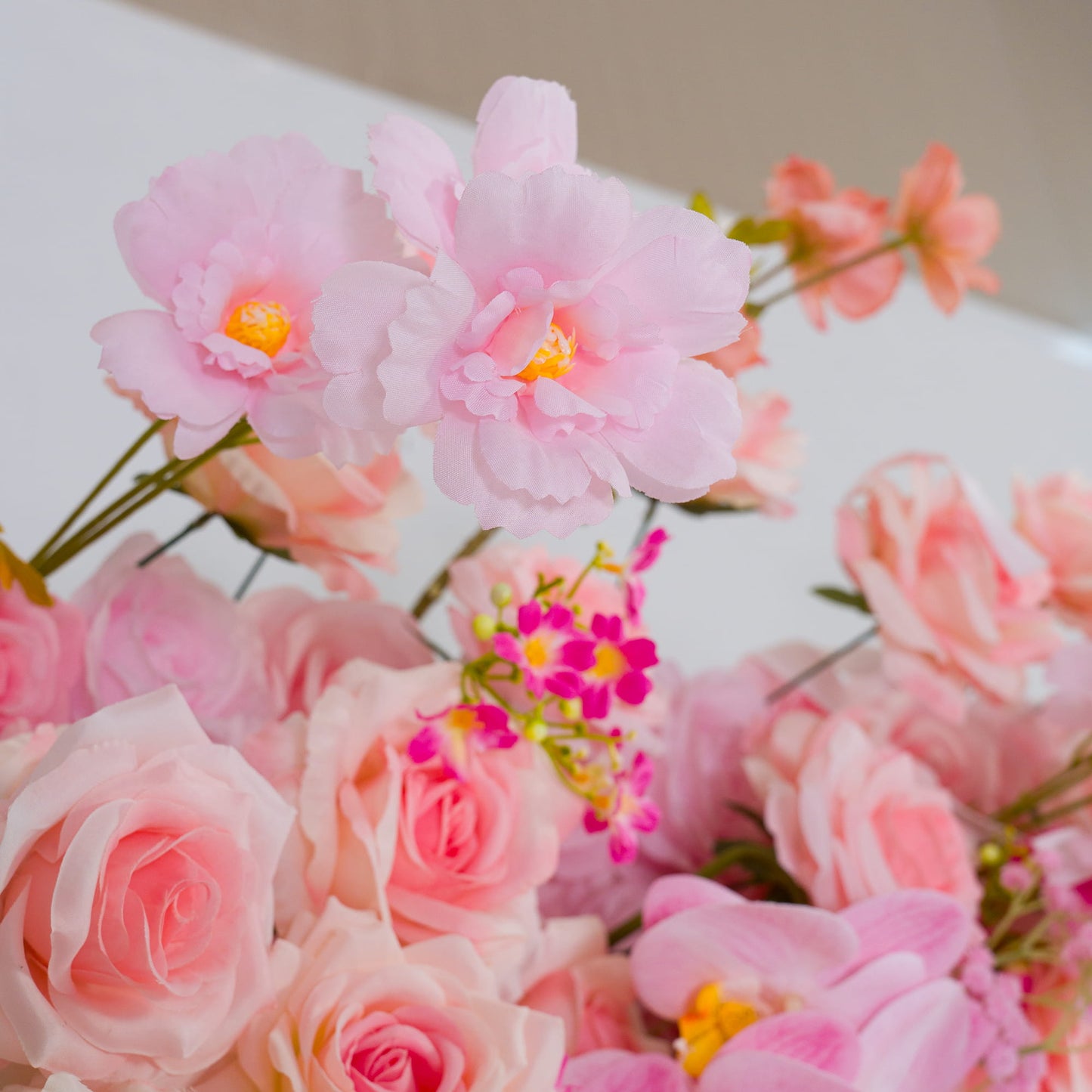 This backdrop showcases a delightful mix of artificial flowers. There are soft - pink roses with their classic, layered petals, light - pink blooms with prominent yellow centers, and small clusters of vibrant pink and yellow filler flowers. 

The colors range from pale to bright pink, with touches of yellow and green from the leaves. The overall style is romantic and whimsical, making it perfect for events like weddings, bridal showers, or other celebratory occasions. 