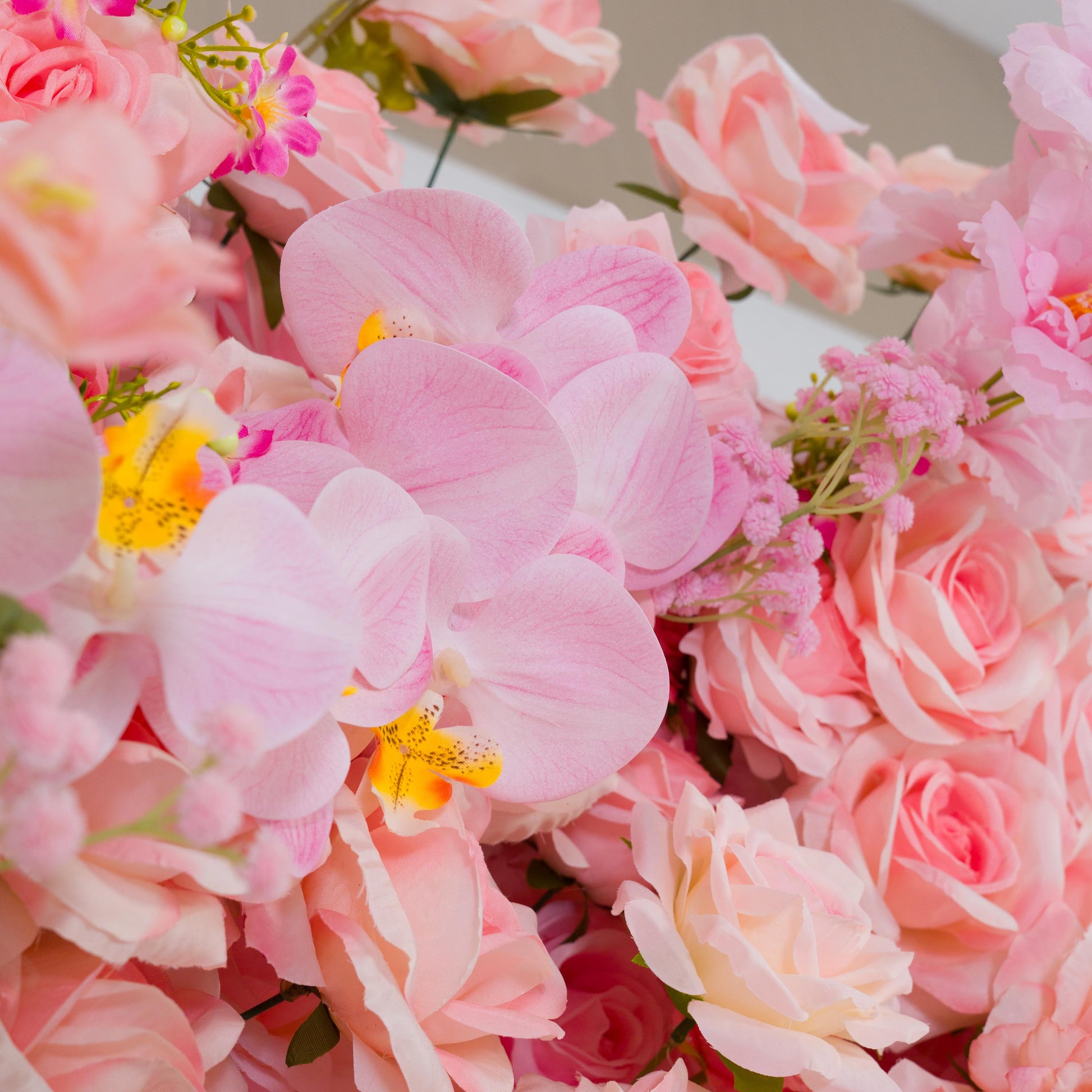 This backdrop features a lush arrangement of artificial flowers. Prominent are soft - pink roses with their classic, ruffled petals, and delicate pink orchids with yellow - spotted centers. There are also small clusters of pink filler flowers adding texture.

The colors span various shades of pink, from pale to vibrant. The overall style is romantic and elegant, making it ideal for events like weddings, bridal showers, or other celebratory functions. 