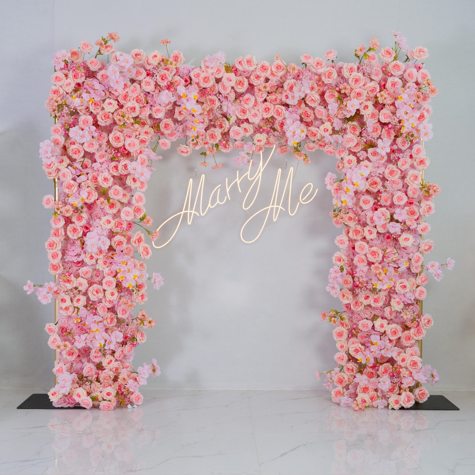 This backdrop is a floral archway densely packed with artificial flowers. The main flowers are pink roses, accompanied by other pink - hued blooms like peony - like flowers. The colors range from soft pastel pinks to slightly deeper shades, creating a harmonious and romantic palette.

A golden - lit "Marry Me" sign is prominently displayed in the center, adding a touch of elegance and romance. The overall style is dreamy and perfect for romantic events such as proposals, weddings, or engagement parties. 