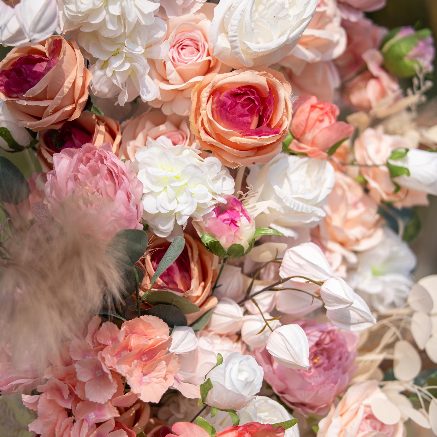 This close - up photo shows a floral arrangement with roses and peonies in soft pink, peach, and white hues. Eucalyptus leaves and pampas grass add texture. Against a blurred green backdrop, it's elegant and romantic, ideal for weddings. 