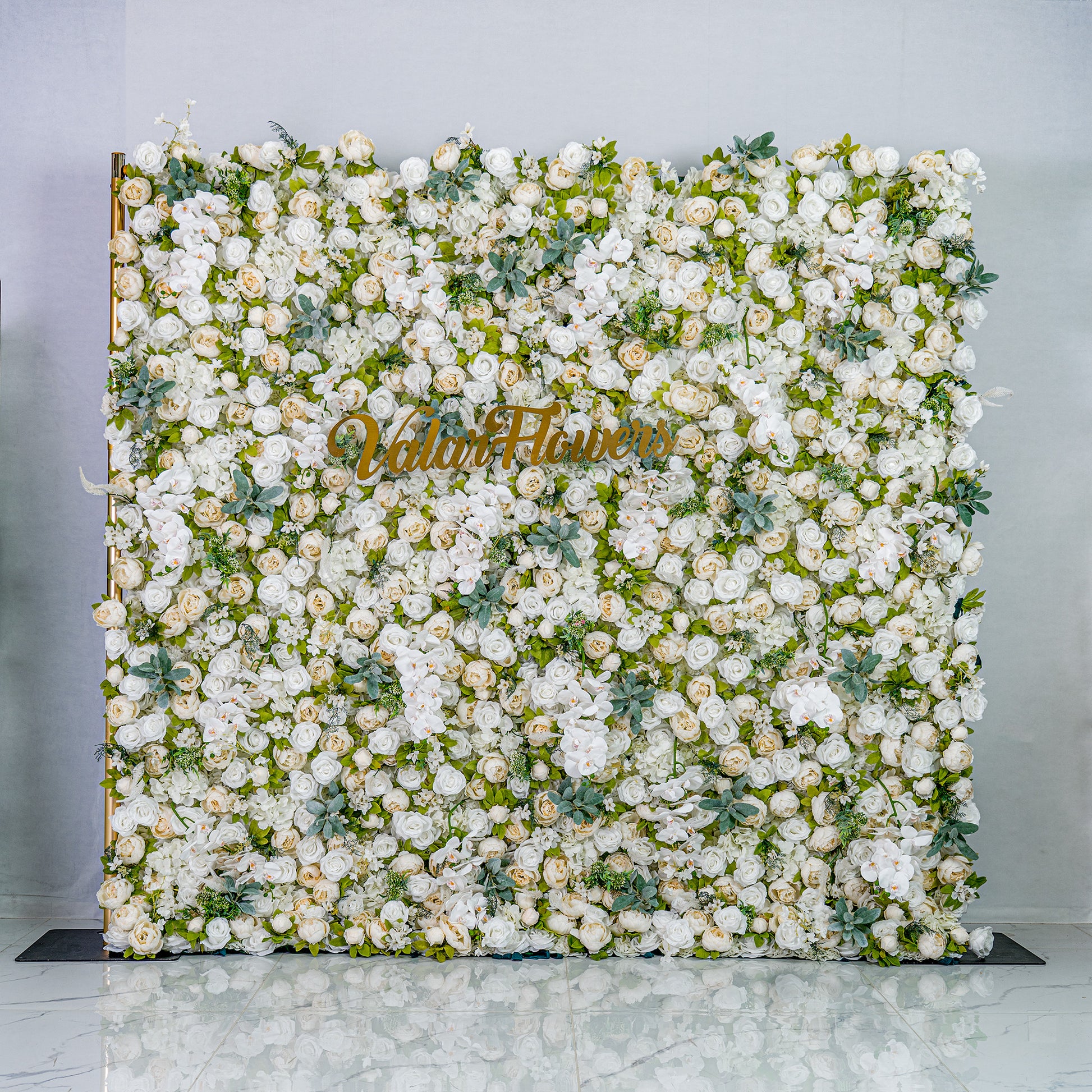 This backdrop is a lush, elegant display of white artificial flowers interspersed with green foliage. Densely packed, it creates a soft, romantic atmosphere. The golden “Valar Flowers” sign adds a touch of sophistication, ideal for weddings or upscale events. 